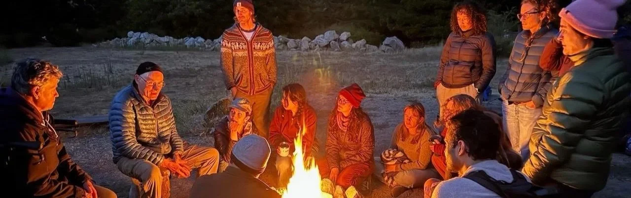 group of people sitting around a campfire at night in a field