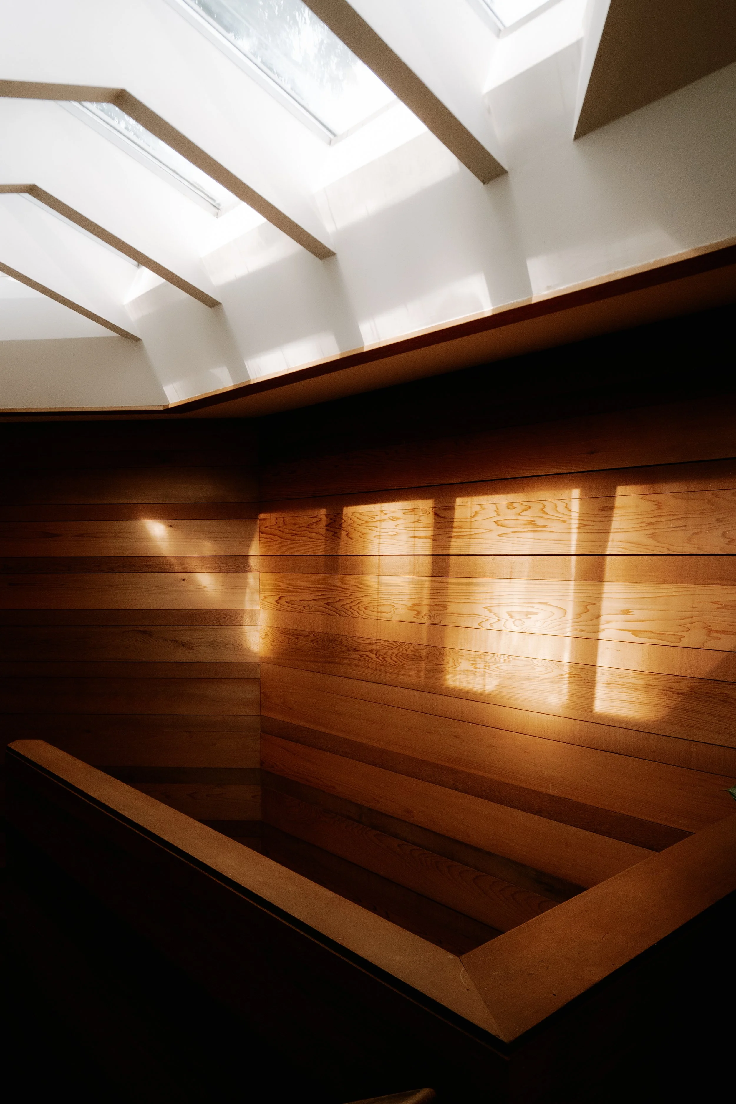 Interior of a house with a wooden staircase and a large window above, allowing natural light to illuminate the space.