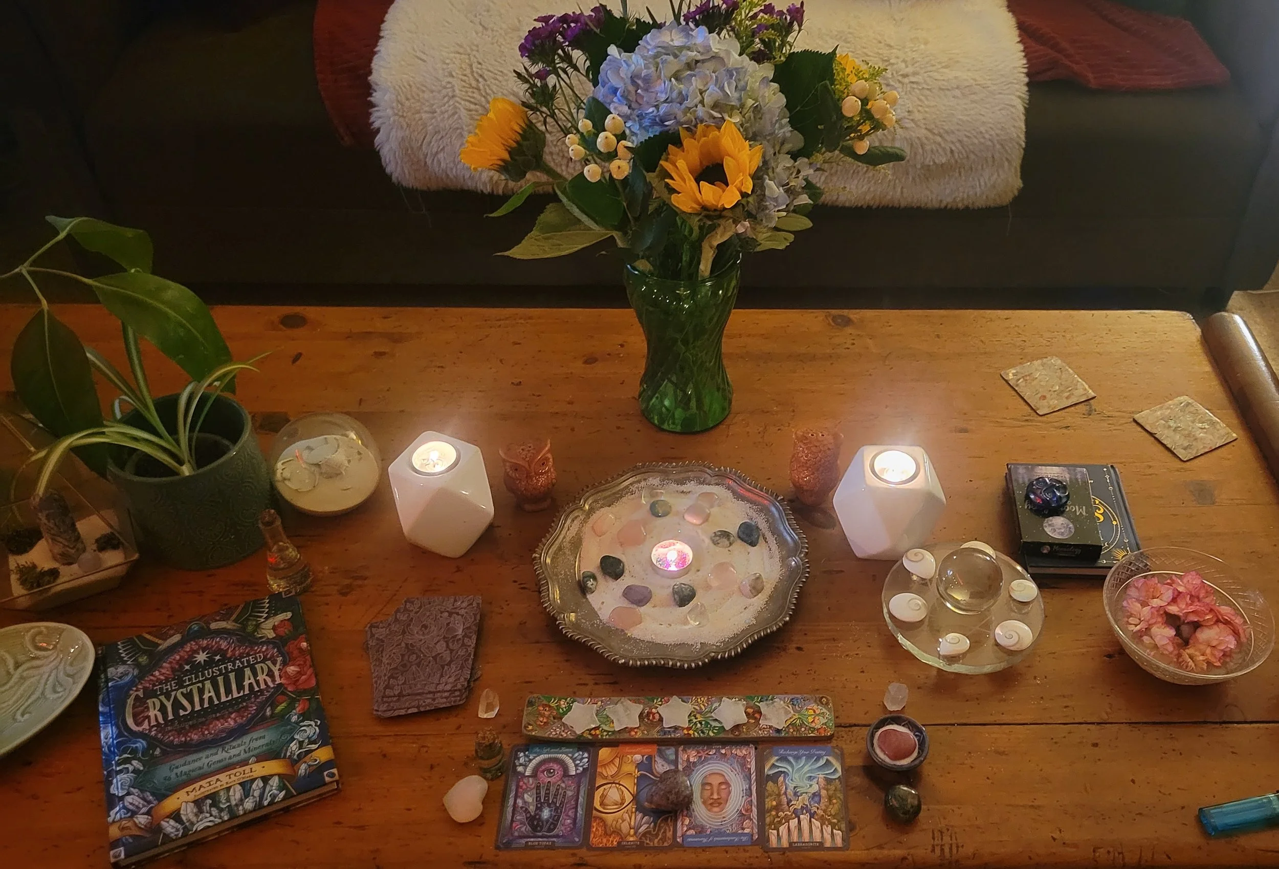 Lit ritual candles surrounded by crystals, books and flowers on a living room coffee table