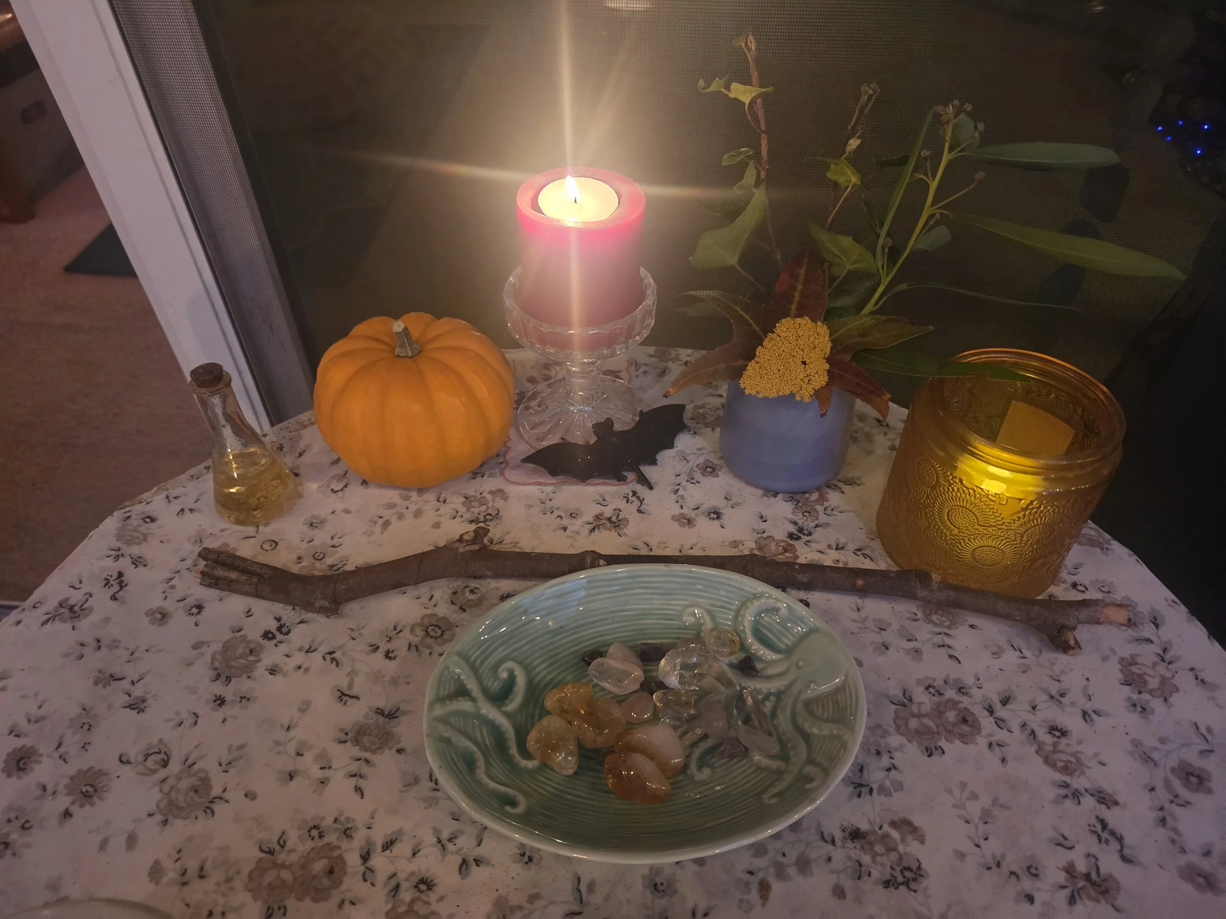 A glowing red candle surrounded by an orange pumpkin, autumn flowers, crystals in a turquoise dish, and seasonal decorations arranged for an October moon intention ritual at the Tree House.