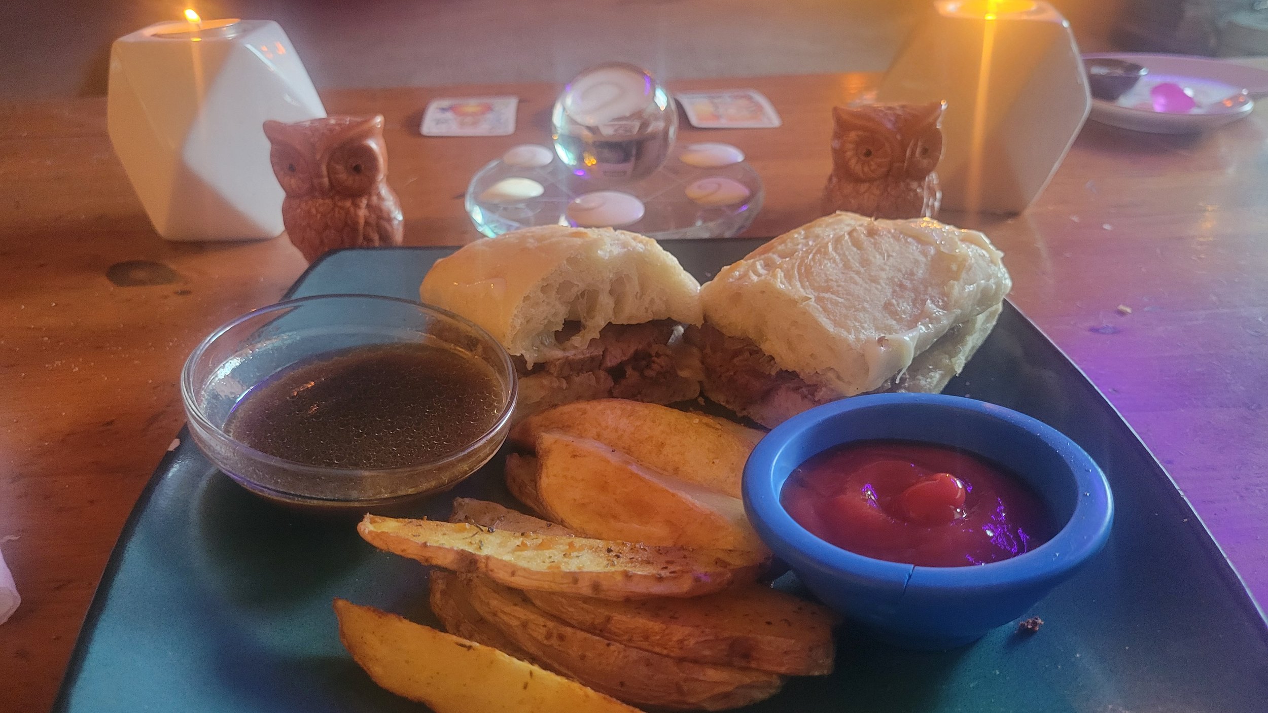French dip sandwich with sliced ribeye and Swiss cheese served with crispy oven fries on a blue plate, with owl salt and pepper shakers in the background.
