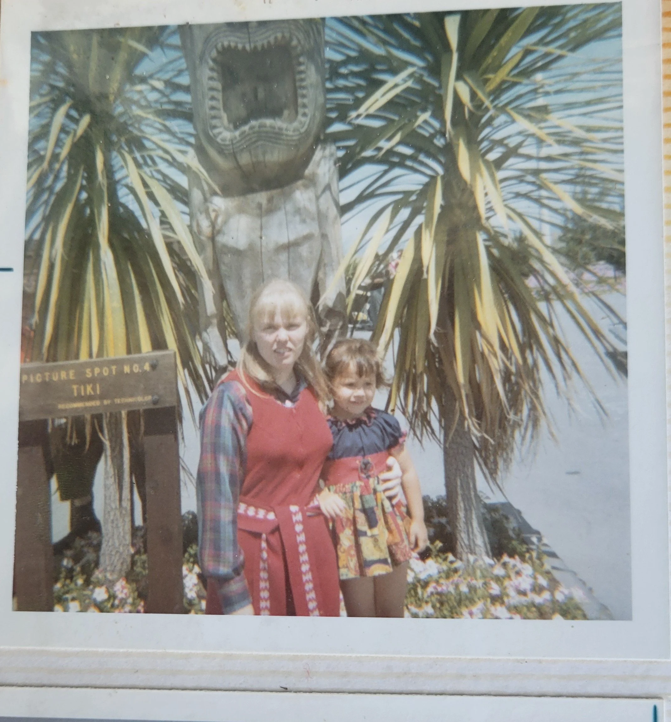 Young girl standing with her mother beside a wooden tiki statue at Tiki Spot No. 4 in San Francisco