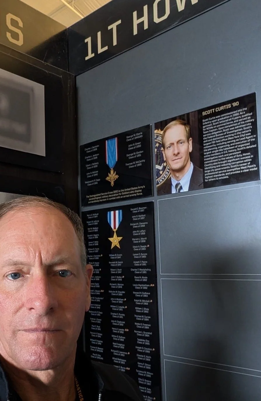 Scott Curtis stands in front of the 1LT Howie Pontuck Wall of Distinction commemorating his induction into the Army Gymnasts Hall of Fame.