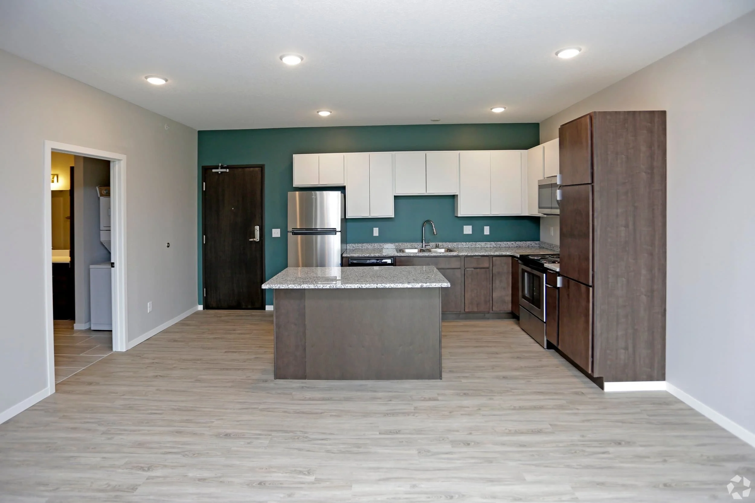 Modern kitchen with brown cabinets, stainless appliances, and island; open to laundry—perfect for apartments in Rochester living.