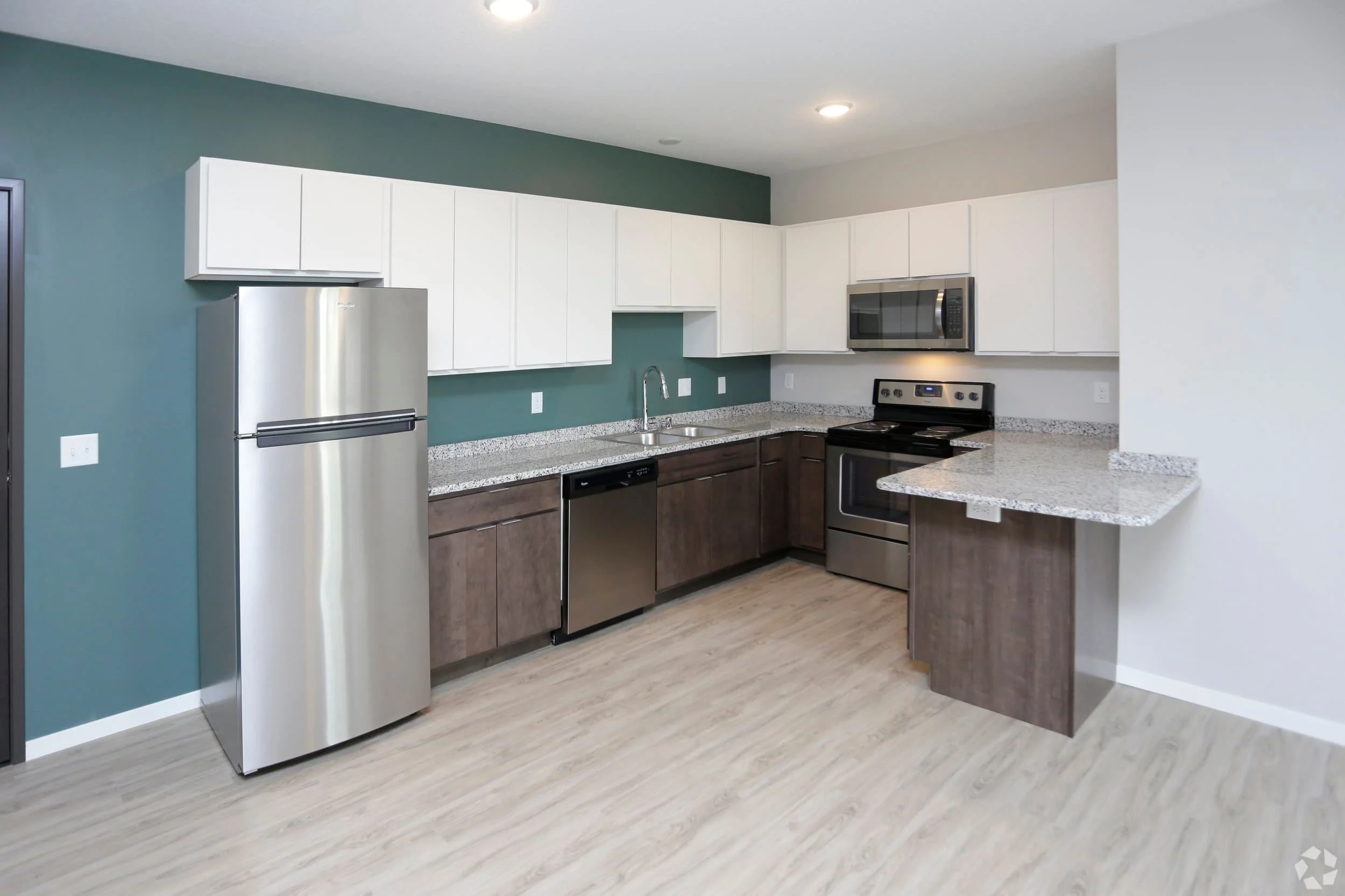 Modern kitchen in apartments in Rochester with stainless steel appliances, white cabinets, granite countertops, and wood flooring.