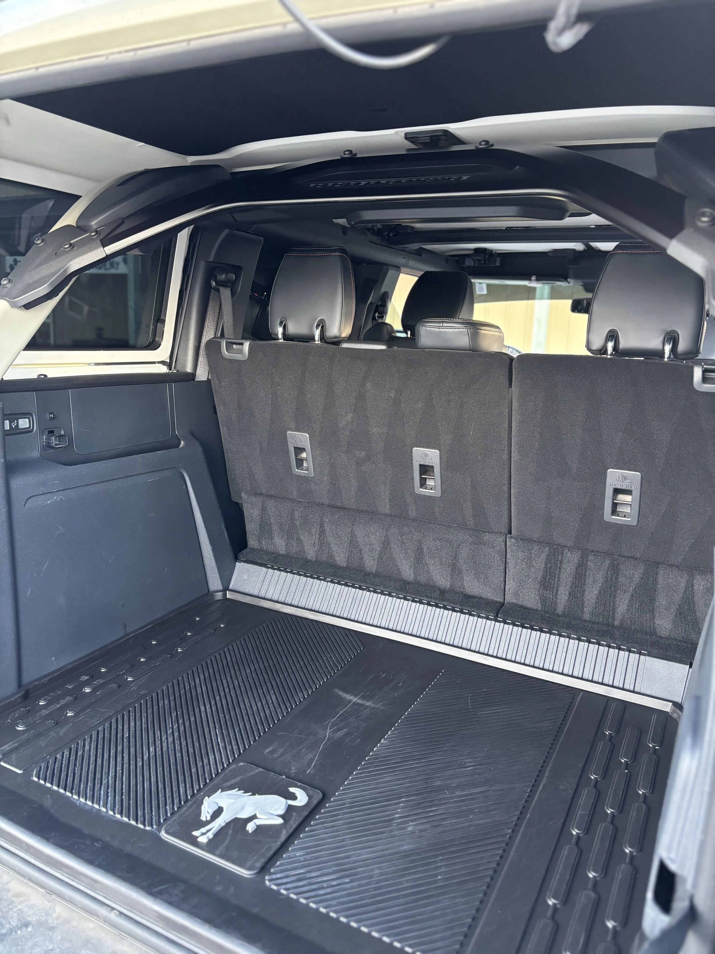 Interior of a vehicle's trunk, showing a black cargo mat with a silver panther emblem, and the back of folded rear seats.
