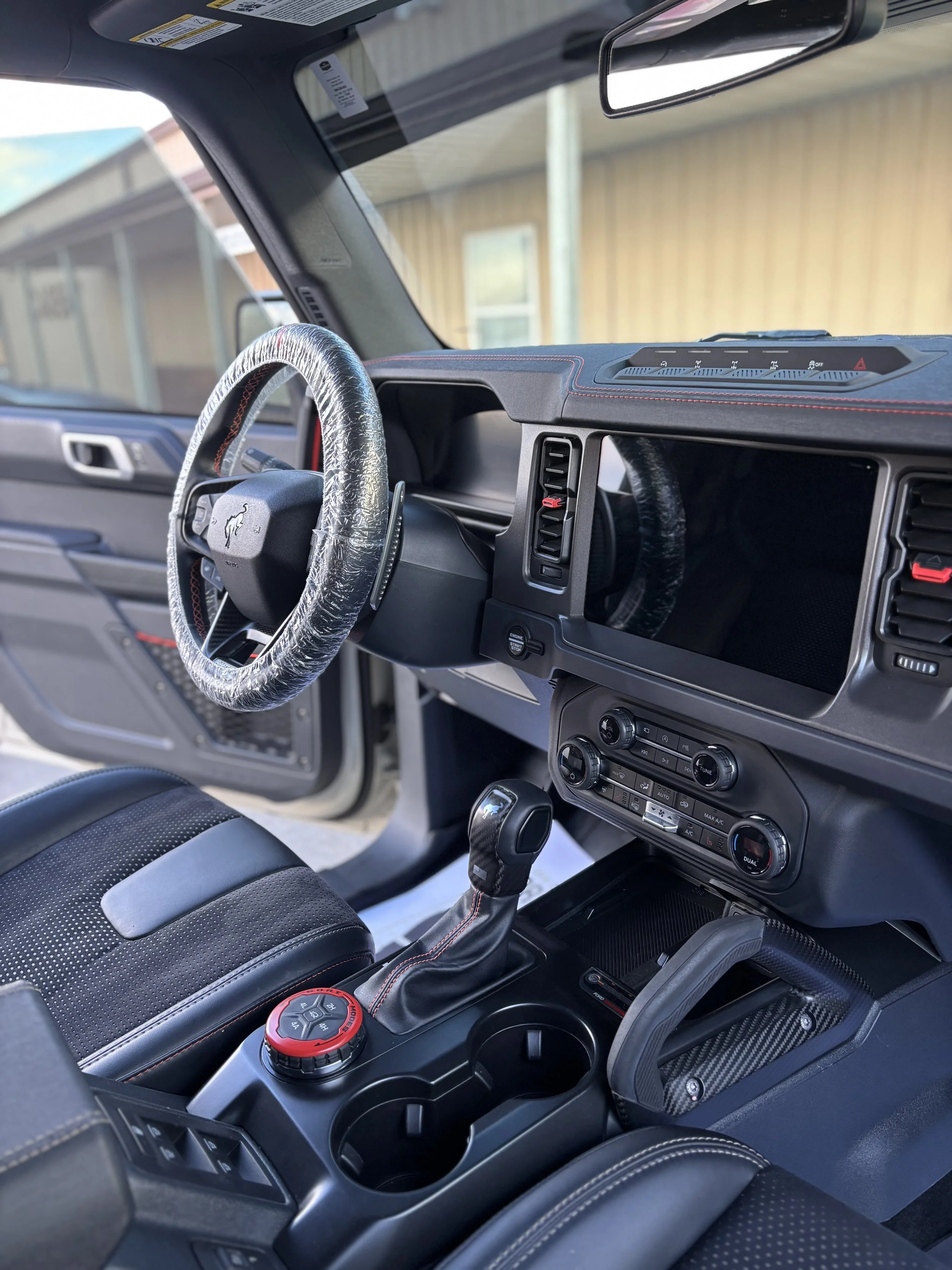 Interior of a car showing the dashboard, steering wheel with a cover, gear shift, and center console with cup holders.