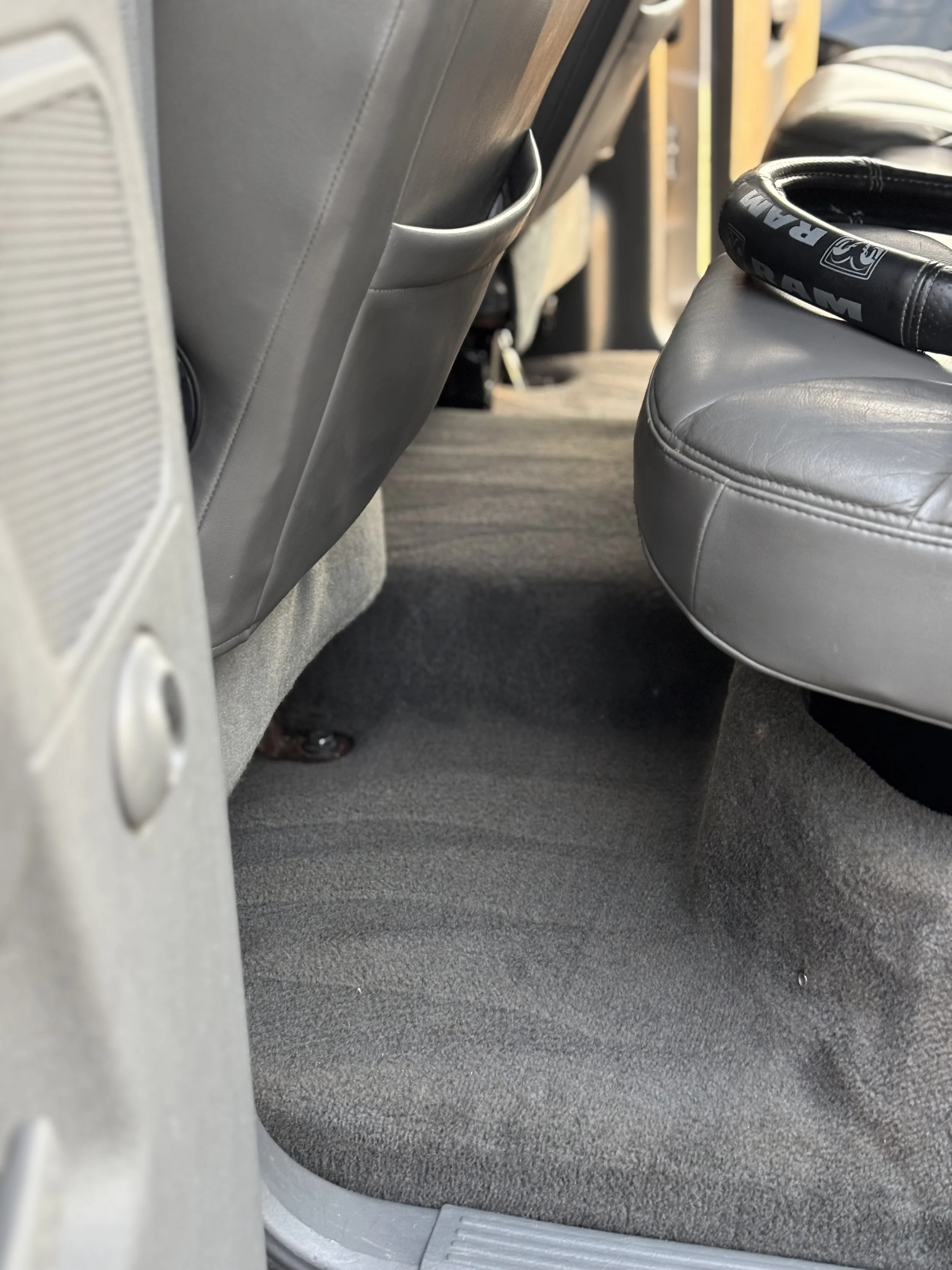 Inside the back seat area of a vehicle showing gray carpeting, the backs of two front seats, and a gray tennis racquet placed on the passenger seat.