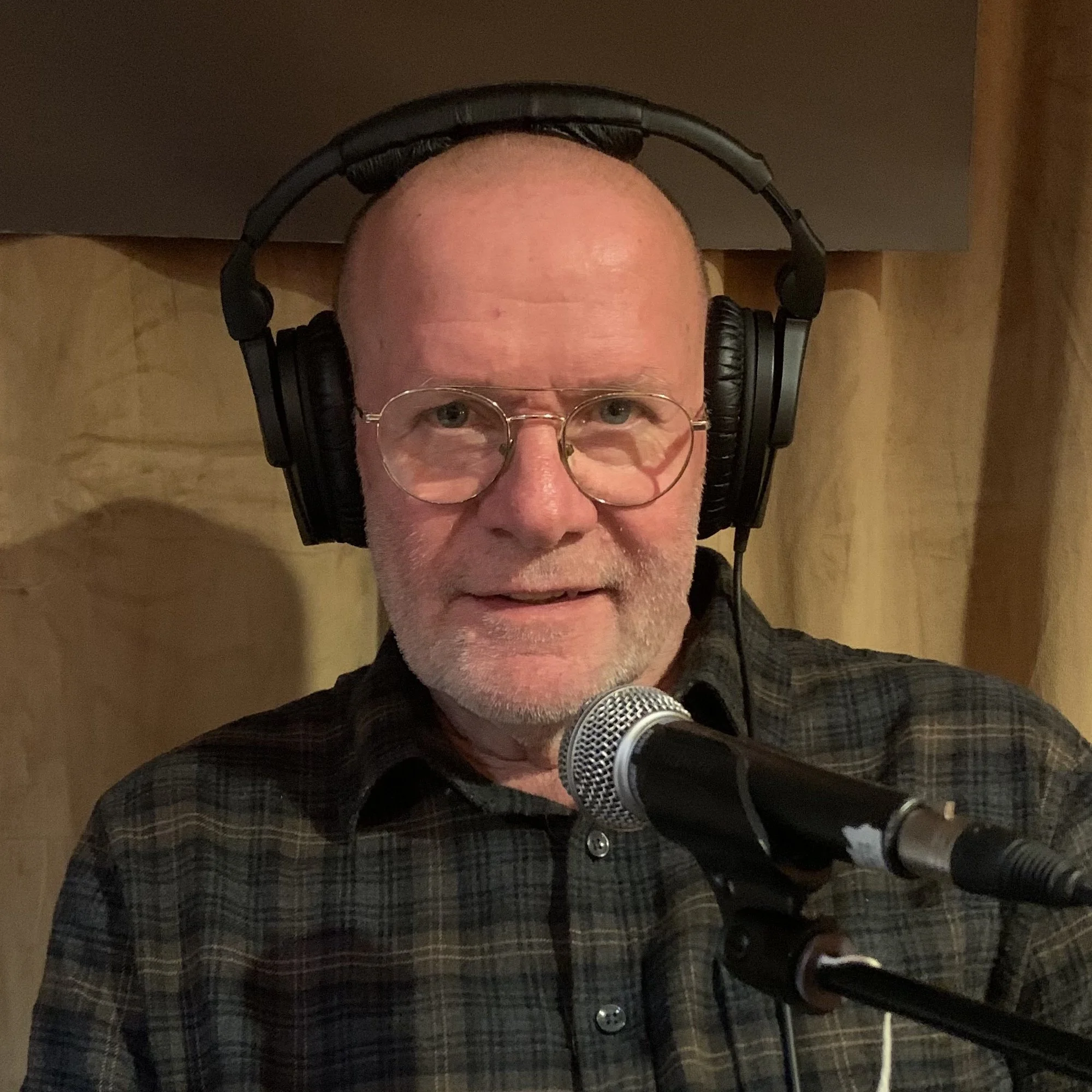 Person med hodetelefoner som sitter foran en mikrofon i et innspillingsmiljø, med dempet bakgrunn og studiolysetting.