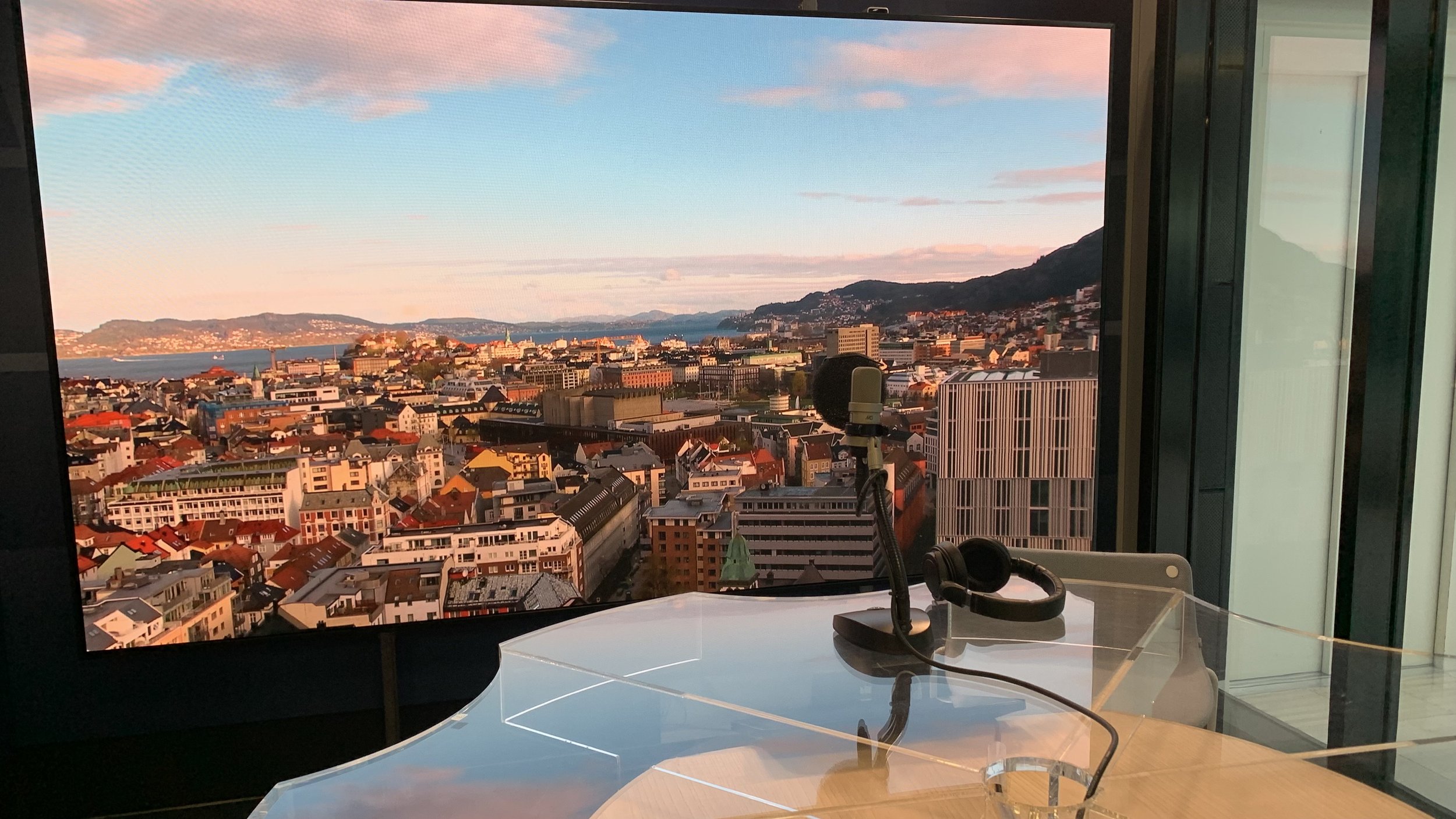 NRK radio‑studio i Media City Bergen med mikrofon og headset foran panoramautsikt over Bergen by.
