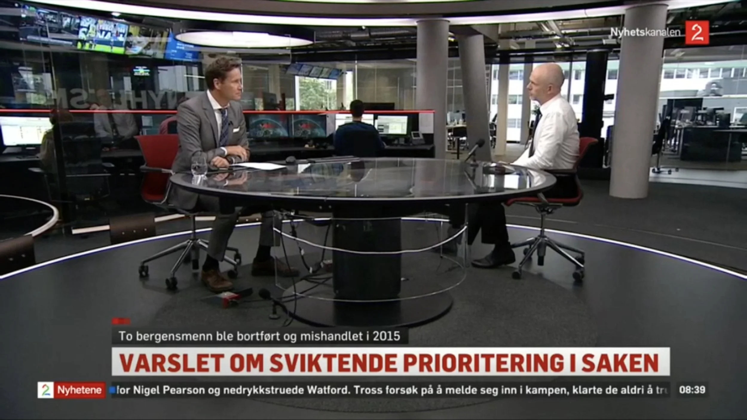TV 2 Nyhetskanalen studio med to personer ved et rundt glassbord under et direktesendt intervju. I bakgrunnen ses nyhetsdesken med skjermer og redaksjonslokale. På skjermen vises teksten «Varslet om sviktende prioritering i saken».