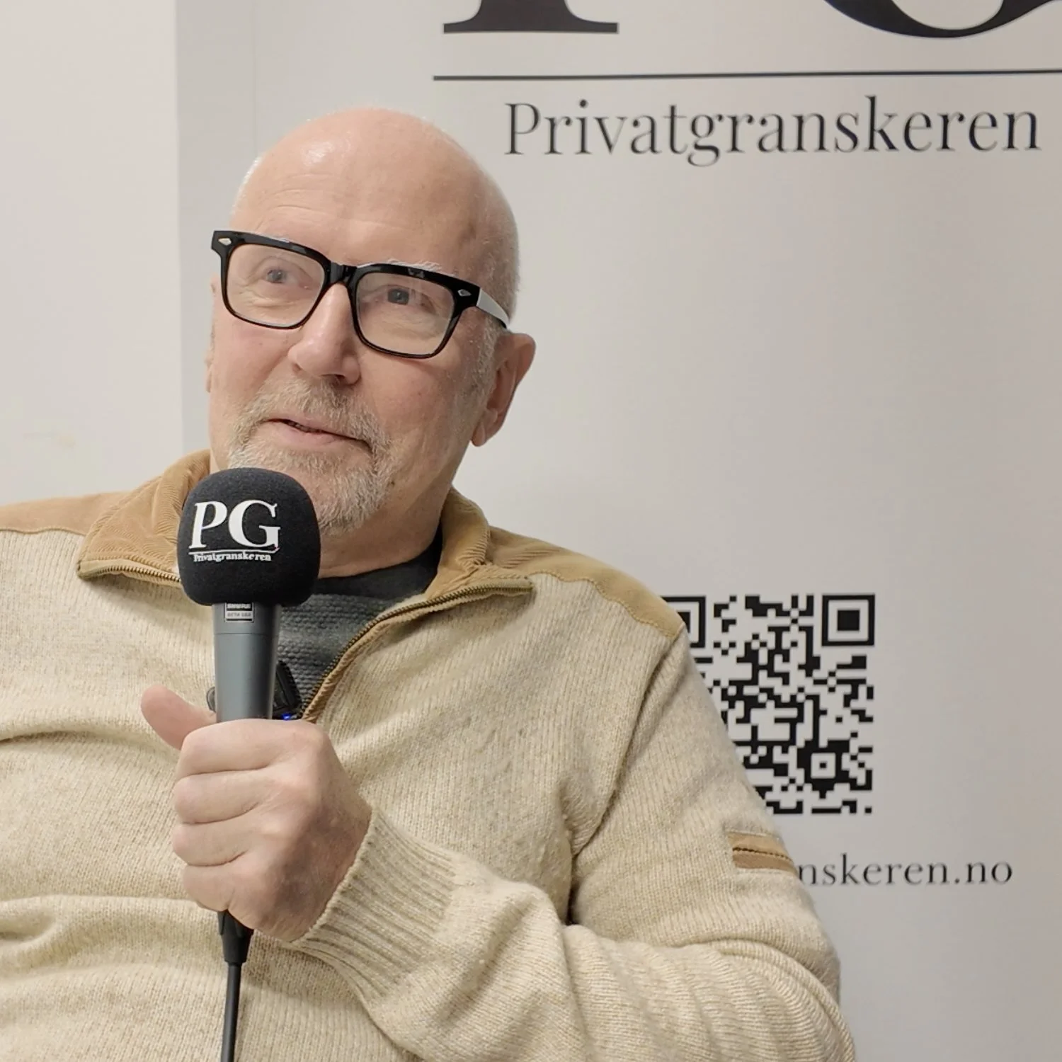 Person sitter i et podkastoppsett og holder en mikrofon med Privatgranskeren‑logo. I bakgrunnen vises et banner med teksten «PG Privatgranskeren» samt en QR‑kode. Personen har på en lys beige genser og sitter mot en nøytral, lys bakgrunn.