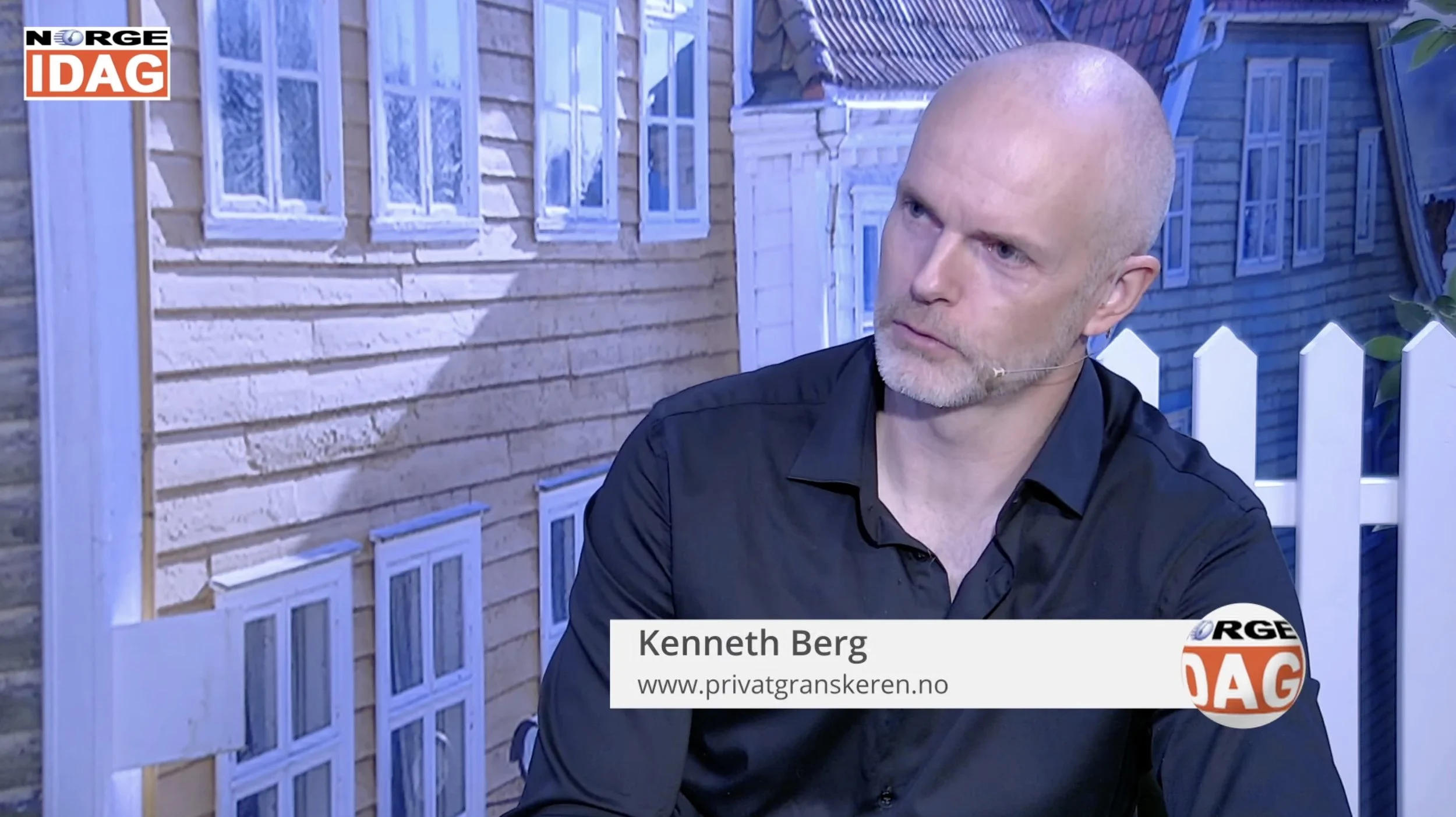 Studioopptak fra Norge IDAG der en person i mørk skjorte sitter ved et bord foran en bakgrunn som viser tradisjonelle trehus med vinduer. På bordet vises en navnestripe med teksten «Kenneth Berg» og nettadressen «www.privatgranskeren.no».