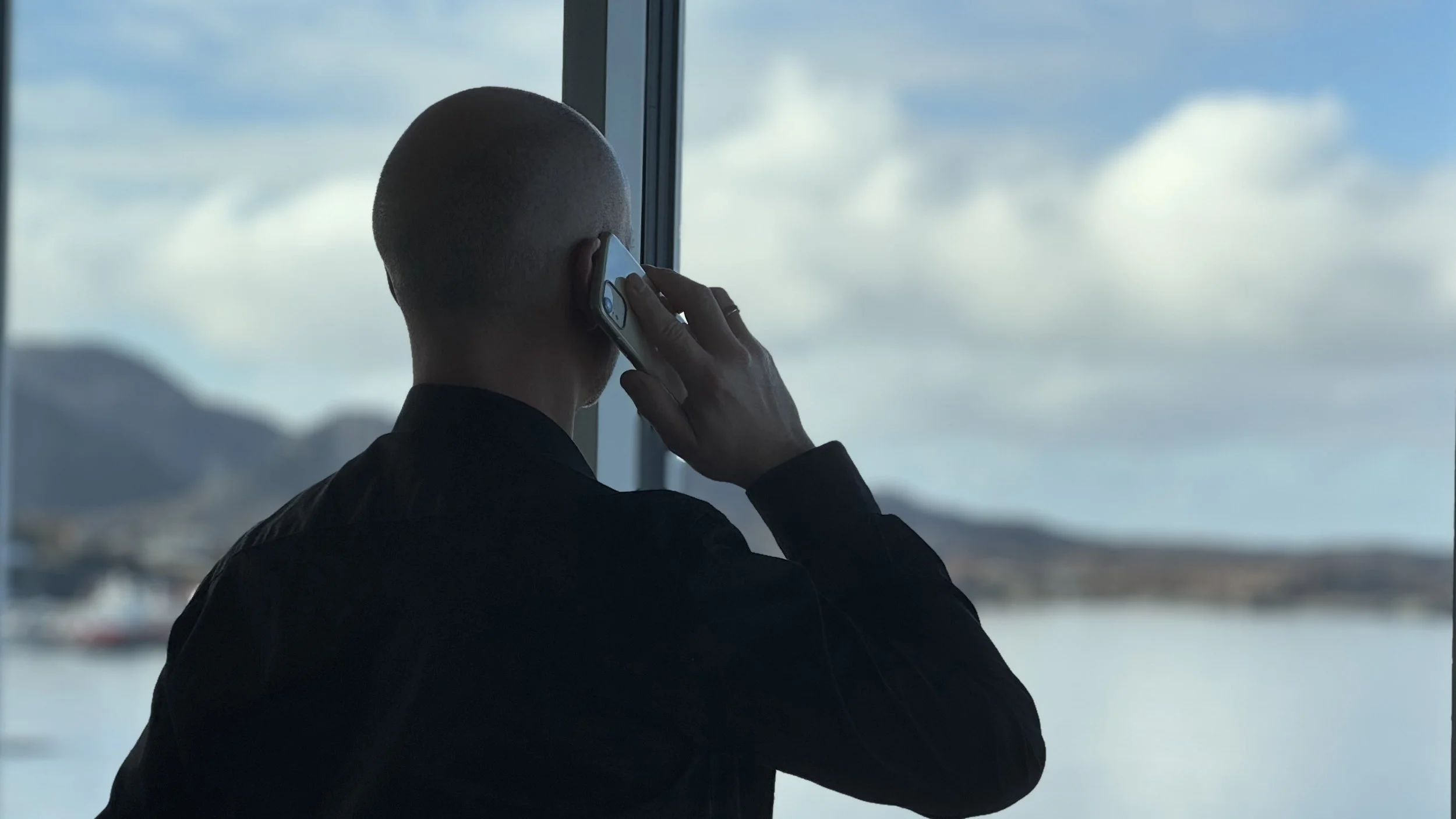 En privat etterforsker fra Privatgranskeren AS står med ryggen til kamera og snakker i telefonen mens han ser ut over et kystlandskap med hav og fjell.