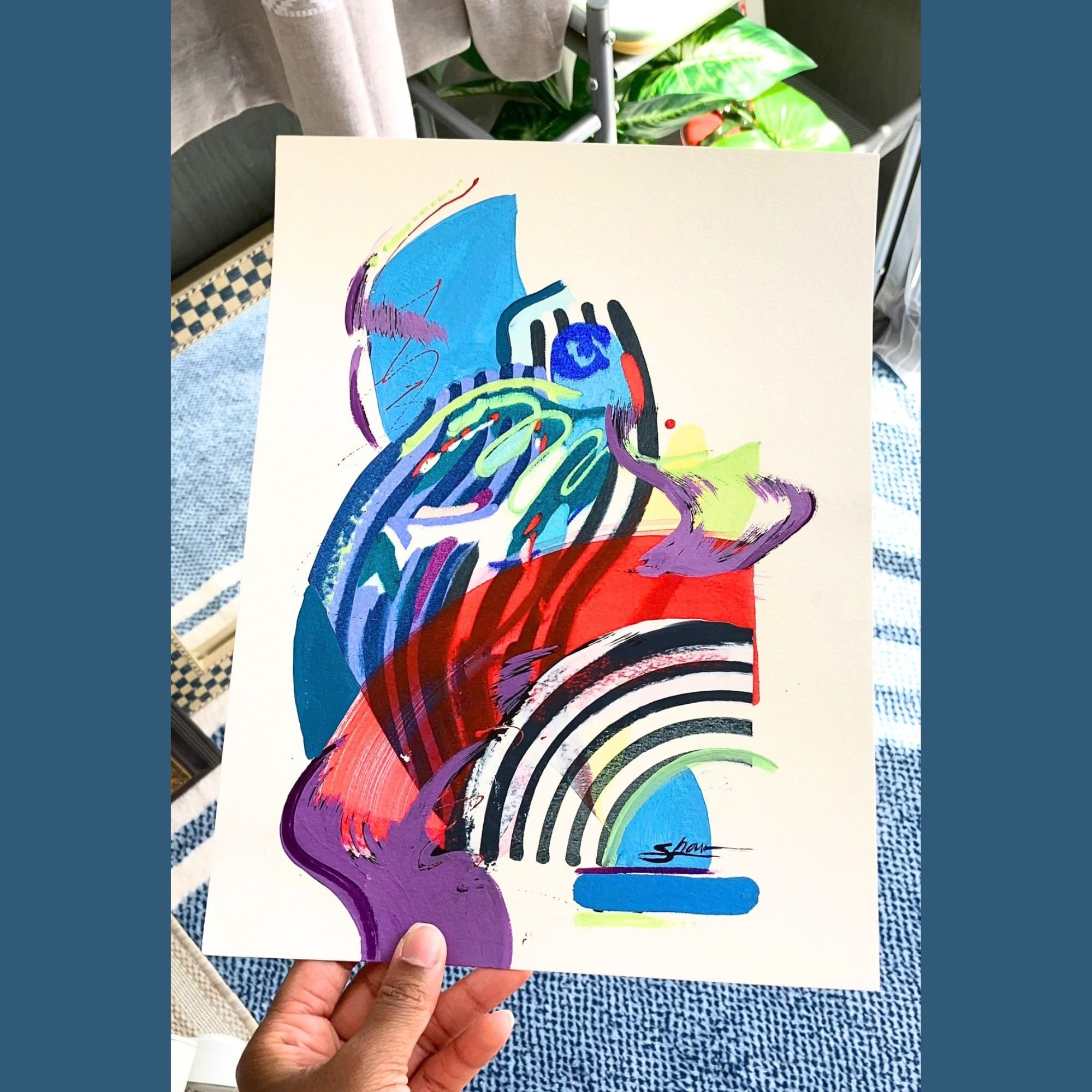 A blue painting with pops of red and other colors. Abstract lines and shapes including stripes and wave like shapes.  Painting shown held in hand with plants and other objects in background.