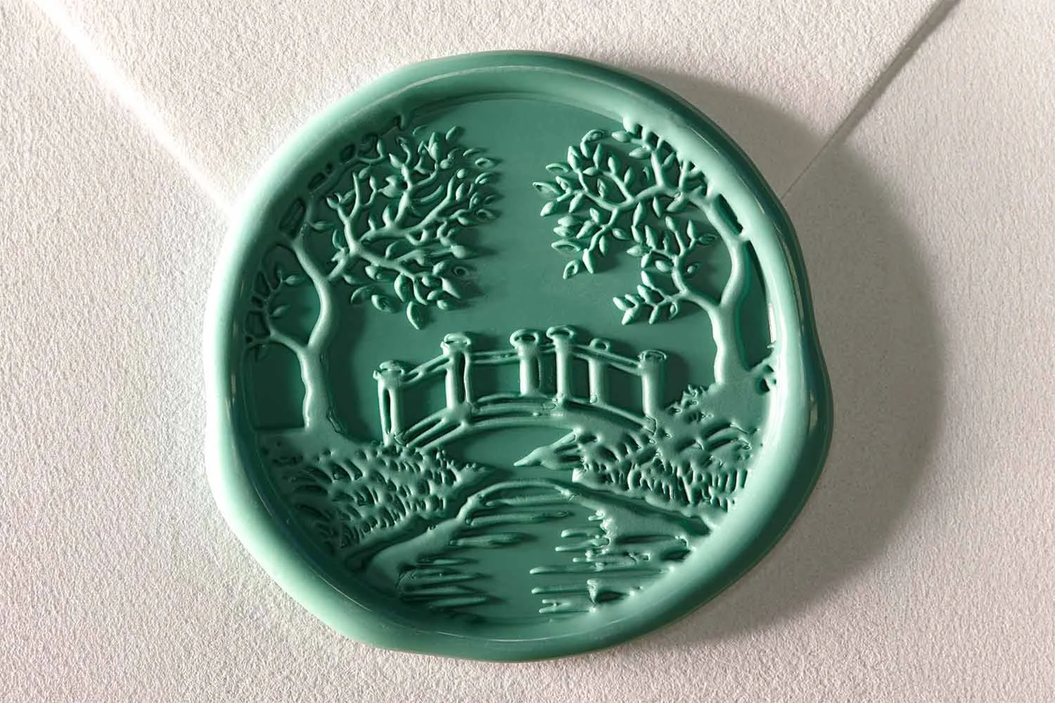 Custom green wax seal with illustrated bridge design attached to luxury wedding invitation envelope.