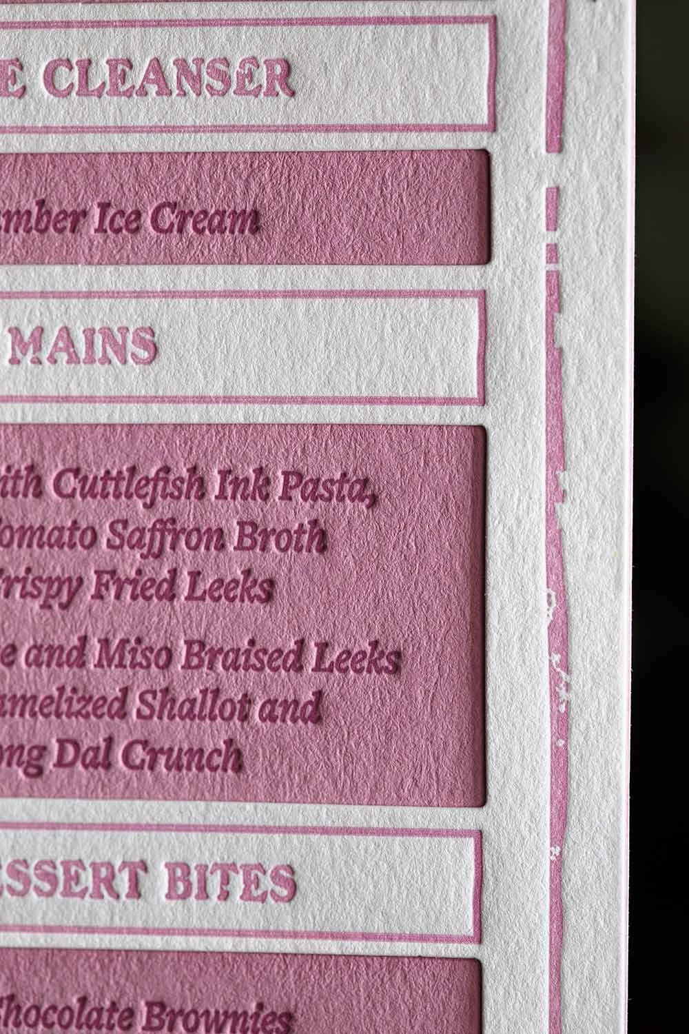 Close-up detail of a letterpress wedding menu showcasing deep impression, layered construction, and textured blush pink paper panels.