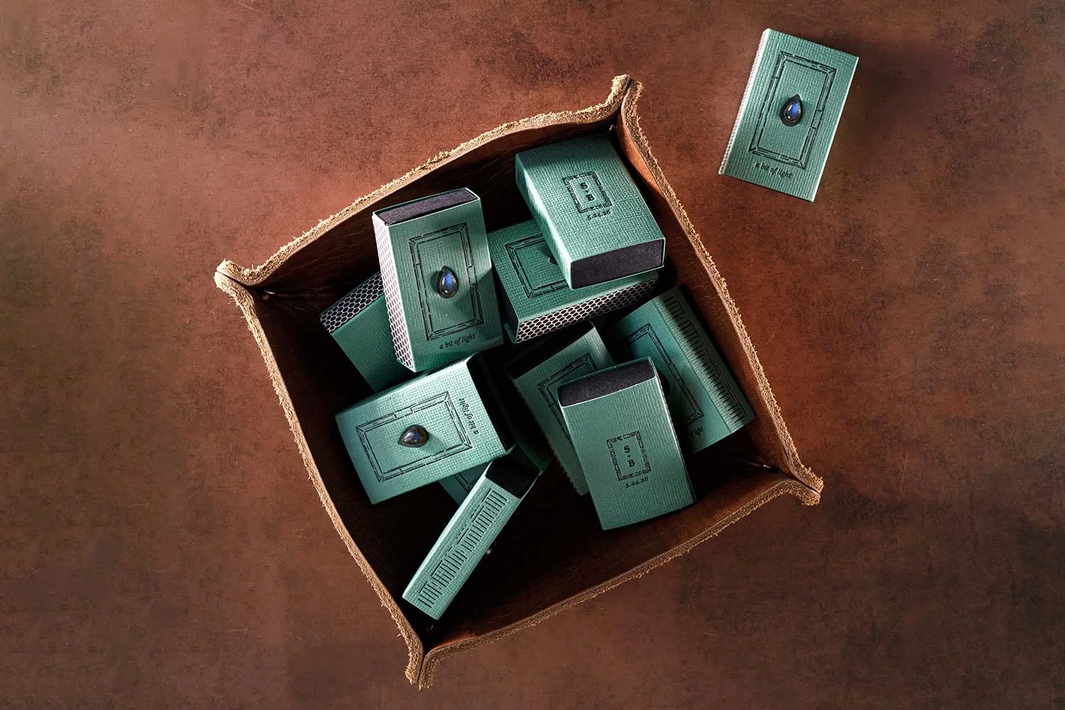 Collection of custom wedding matchbox favors with labradorite gemstones, letterpress details, and textured paper packaging designed for a luxury wedding celebration.