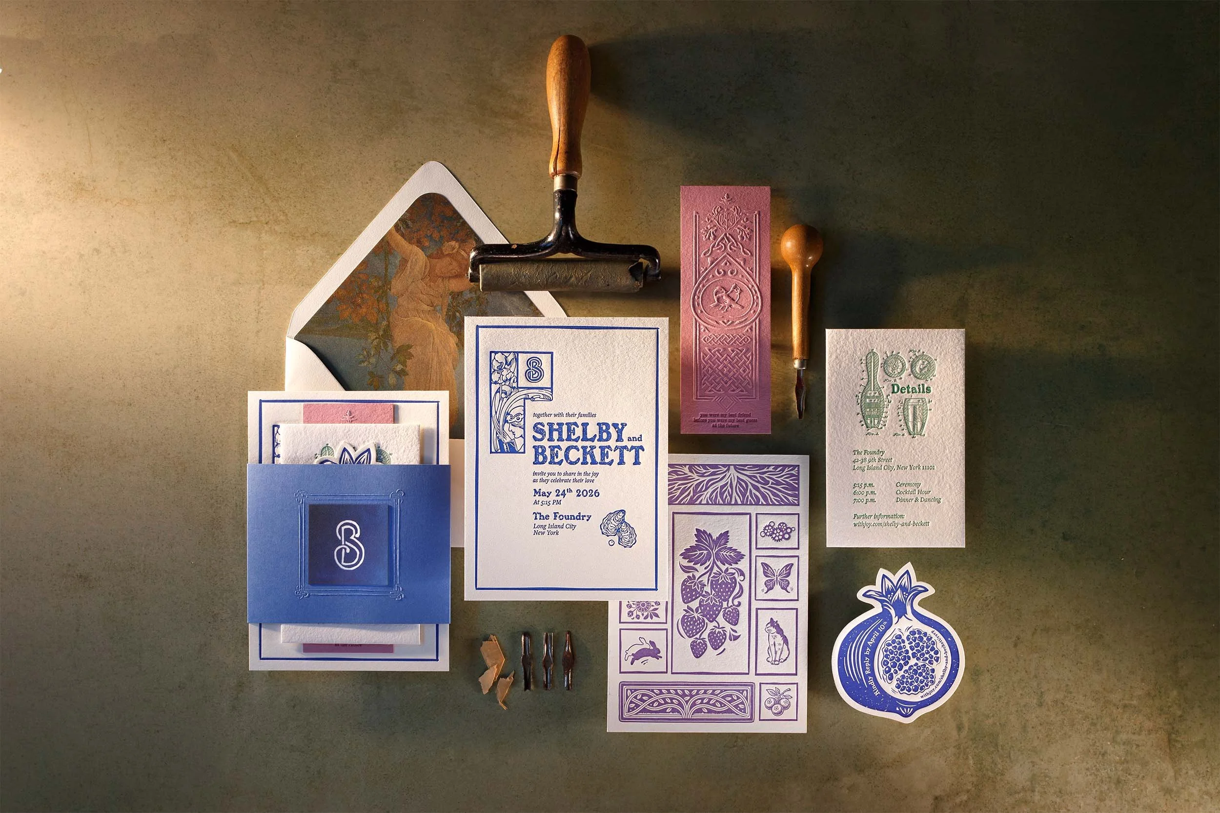 Custom letterpress wedding invitation flat lay with blue and pink art-forward stationery suite, embossed details, vintage printmaking tools, and illustrated envelope liner by Lucasano Creative.