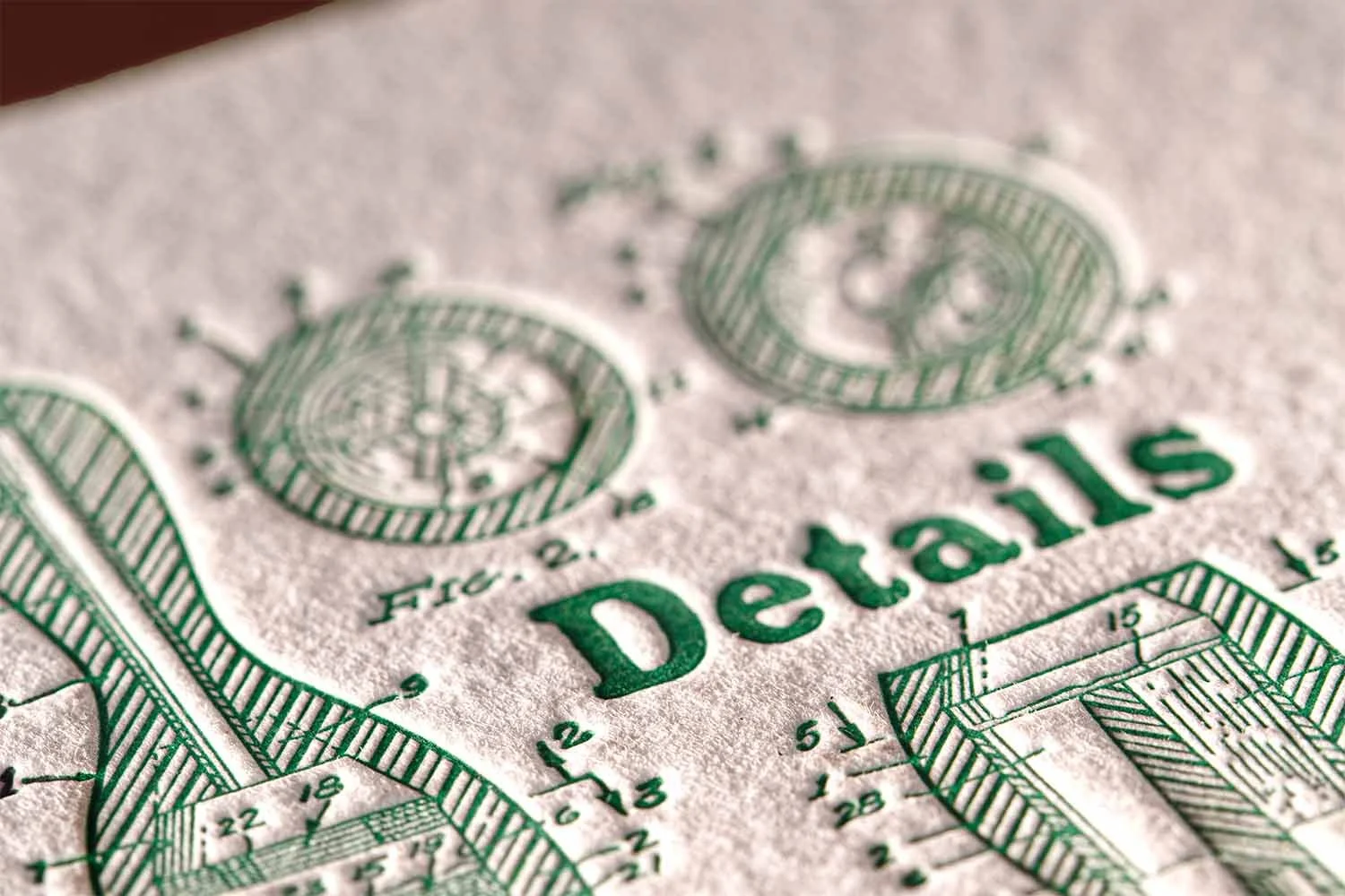 Macro detail of green letterpress details card with tactile cotton paper texture and vintage technical artwork.