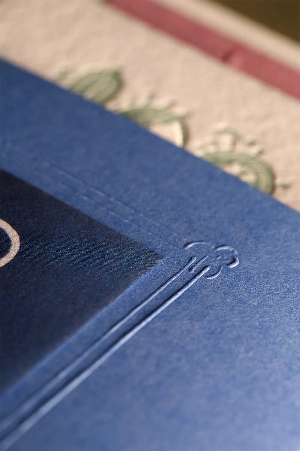 Close-up of blind embossed monogram frame on deep blue wedding invitation belly band with layered stationery underneath.