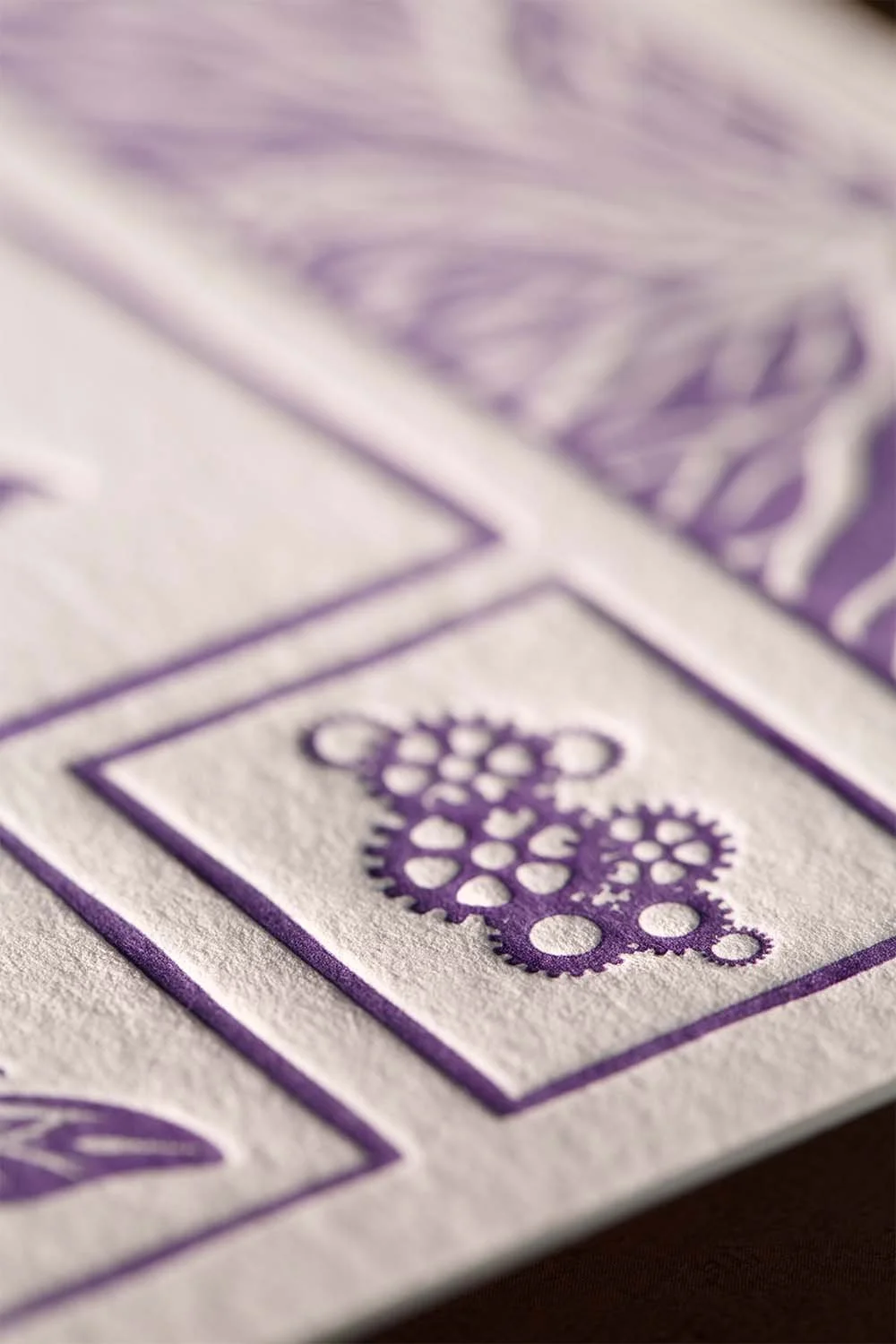 Close-up of purple letterpress illustration detail with textured cotton paper and hand-carved printmaking aesthetic.