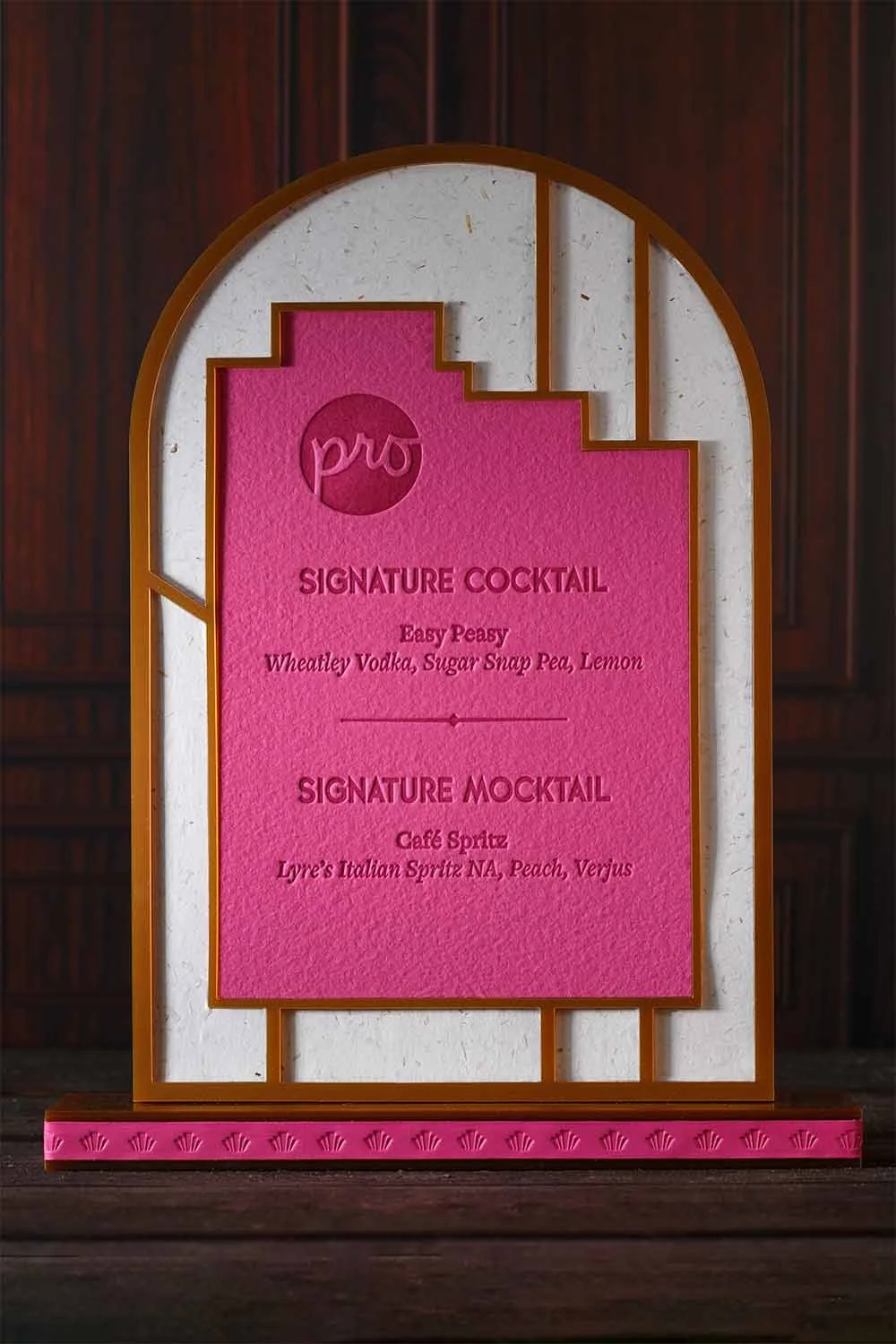 Art Deco-inspired signature cocktail sign with layered acrylic framing, embossed pink paper, and luxury wedding bar signage by Lucasano Creative.