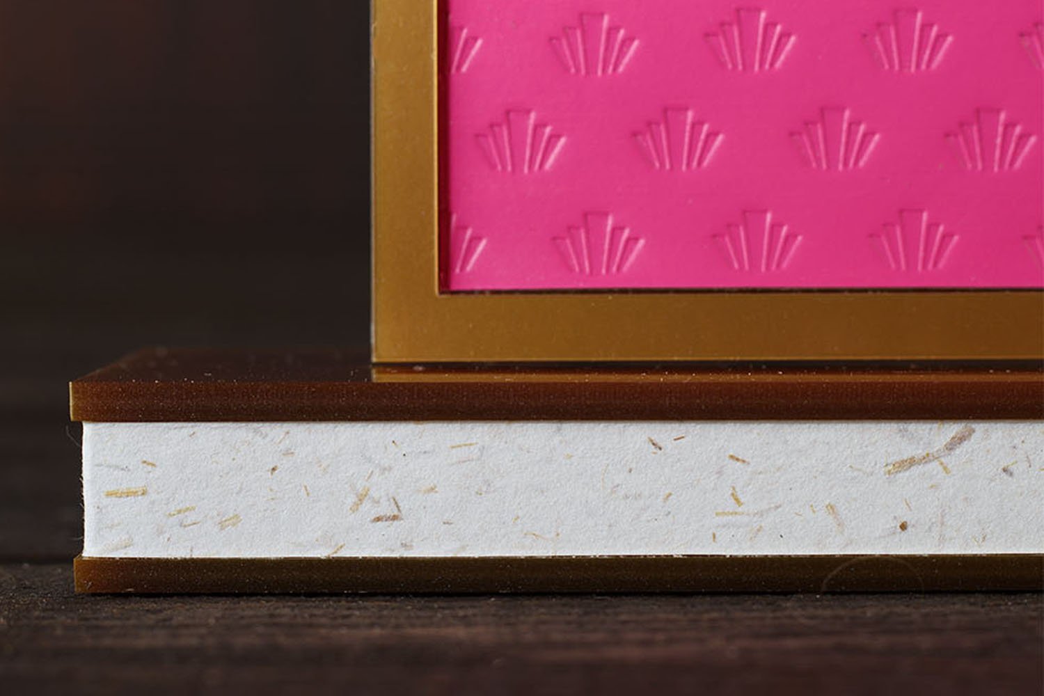 Close-up of layered acrylic event signage base with handmade textured paper and Art Deco-inspired luxury design details. Macro detail of embossed