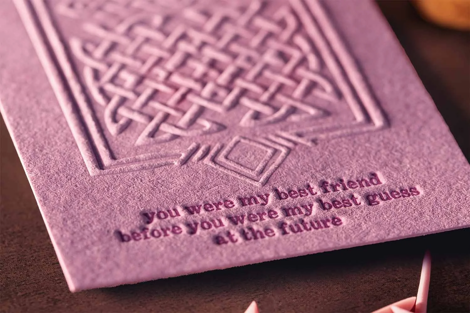 Close-up of blind embossed bookmark featuring tactile Celtic knotwork and deep impression on blush pink paper.