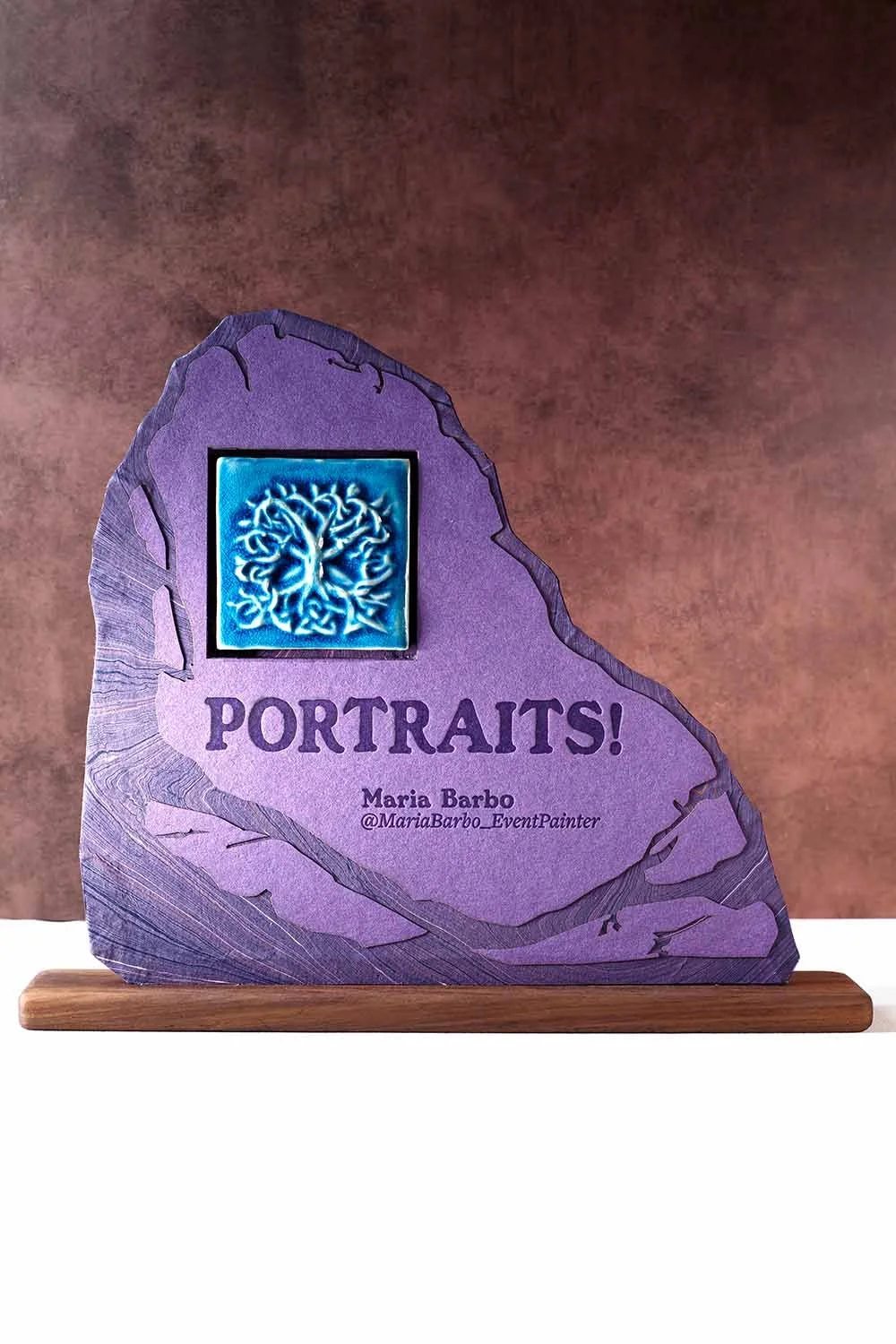 Custom signage for a live wedding painter featuring layered paper artwork, handcrafted ceramic tile detail, and personalized artist information for a wedding reception.
