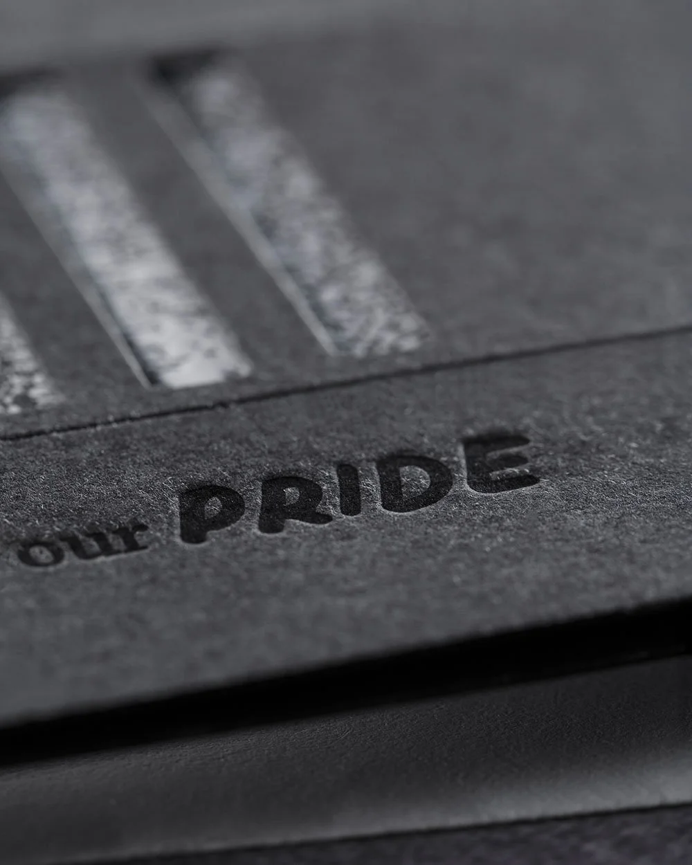 Close-up detail of the word “PRIDE” deeply letterpressed into black paper on the Our Pride Card, highlighting the tactile craftsmanship and texture of the greeting card.