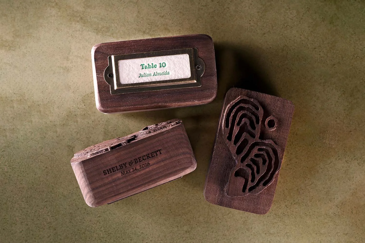 Custom walnut wedding escort card blocks with carved artwork, brass label holders, and personalized guest seating cards for a luxury wedding reception.