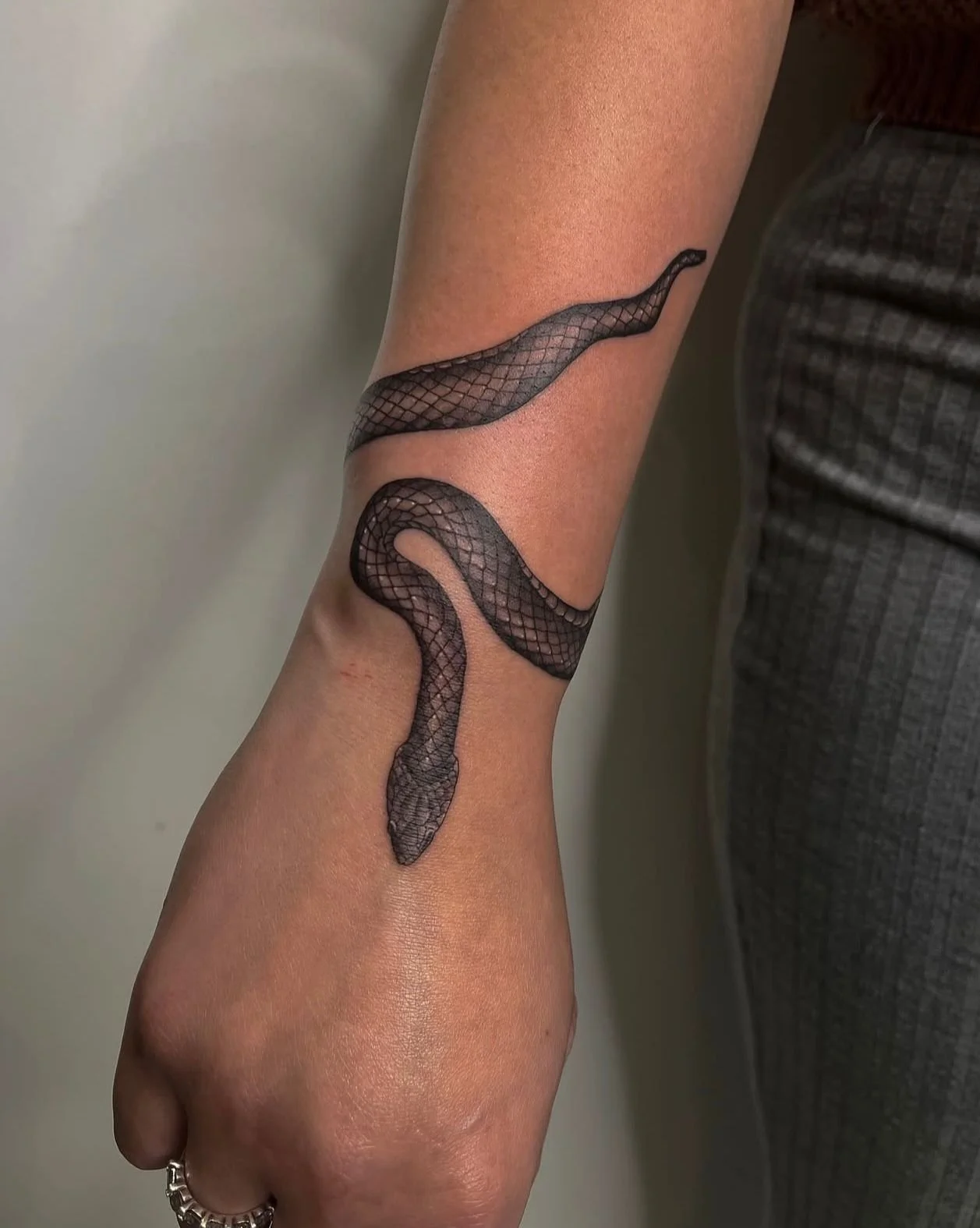 Dark black and grey snake tattoo wrapped around the lower wrist with the head reaching on to the back of the hand.