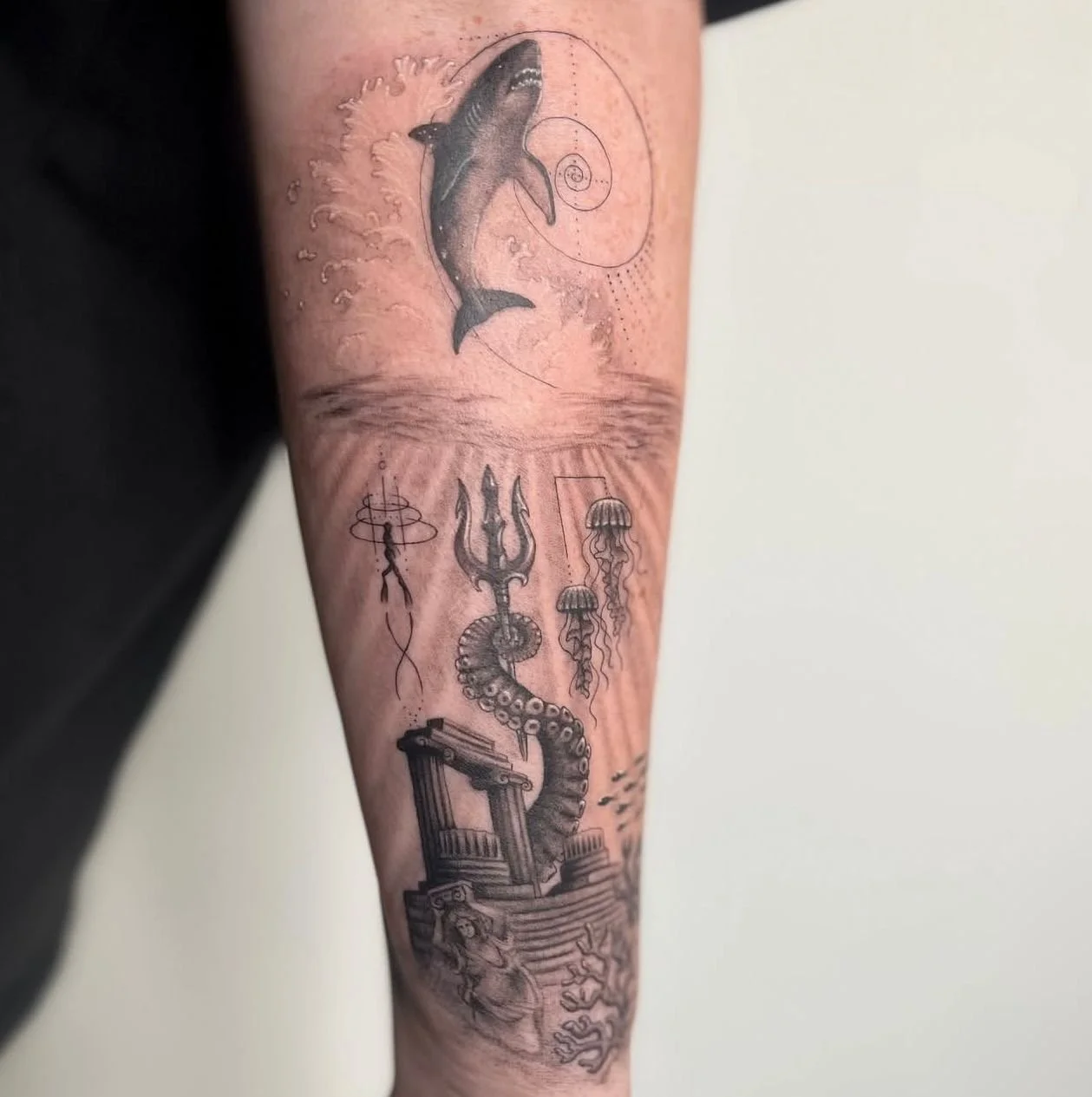 Fineline and fine detailed microrealism black and grey forearm tattoo depicting Atlantis, with a staitcase, trident, giant tentacle, statues, a diver, shark and Golden Ratio.