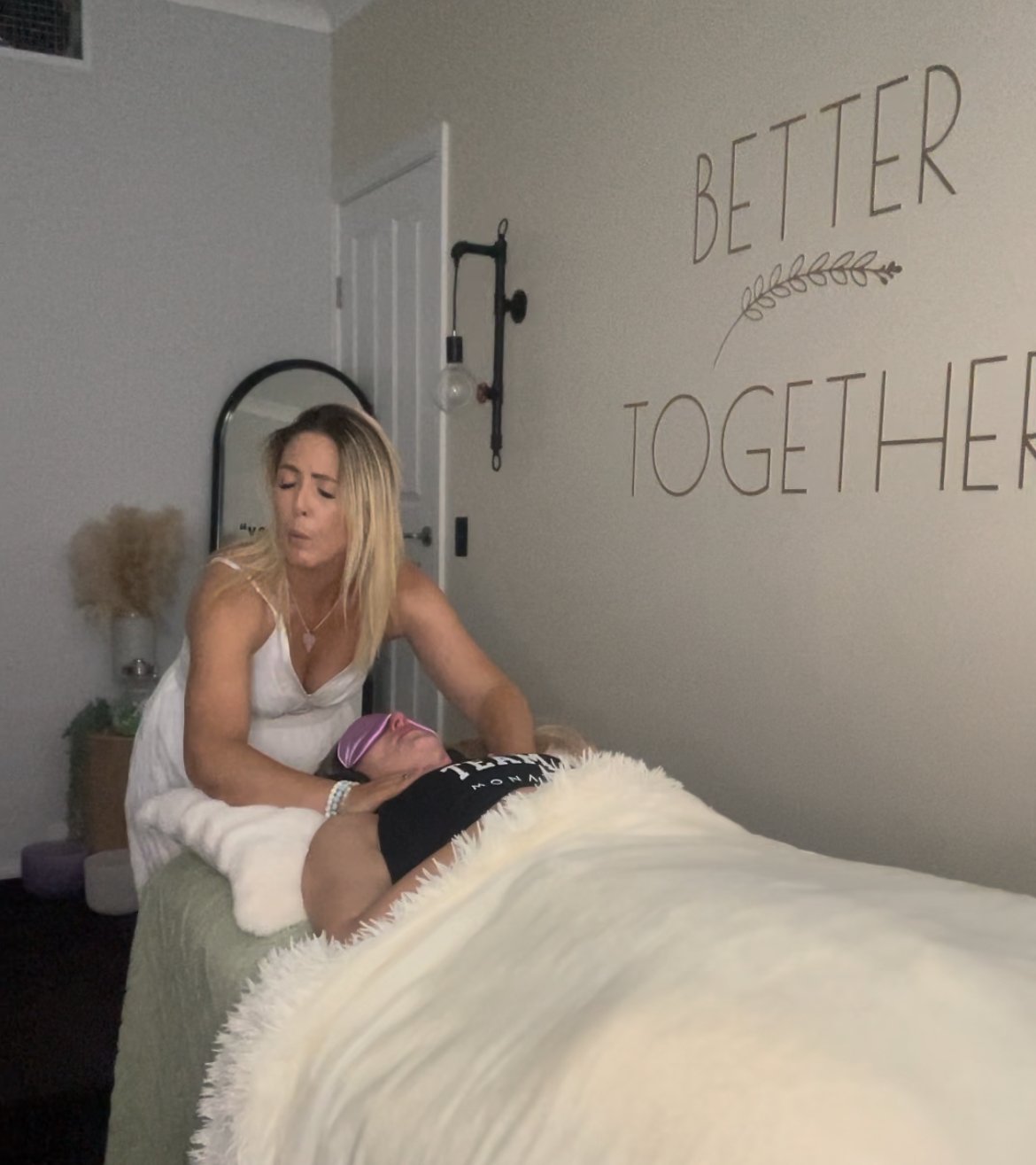 Woman giving a massage to a person lying down in a room with 'Better Together' written on the wall.