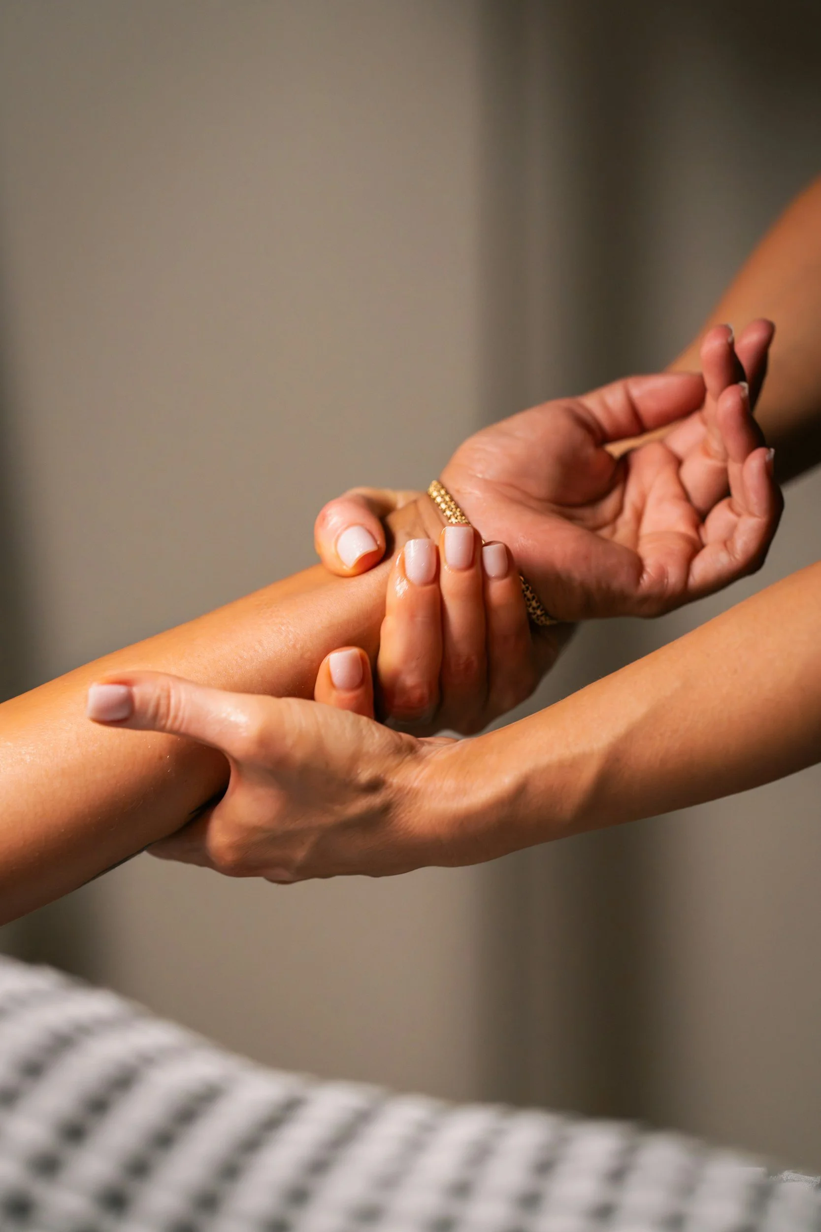 Close-up of two hands holding each other, one hand with a gold ring, against a plain background.