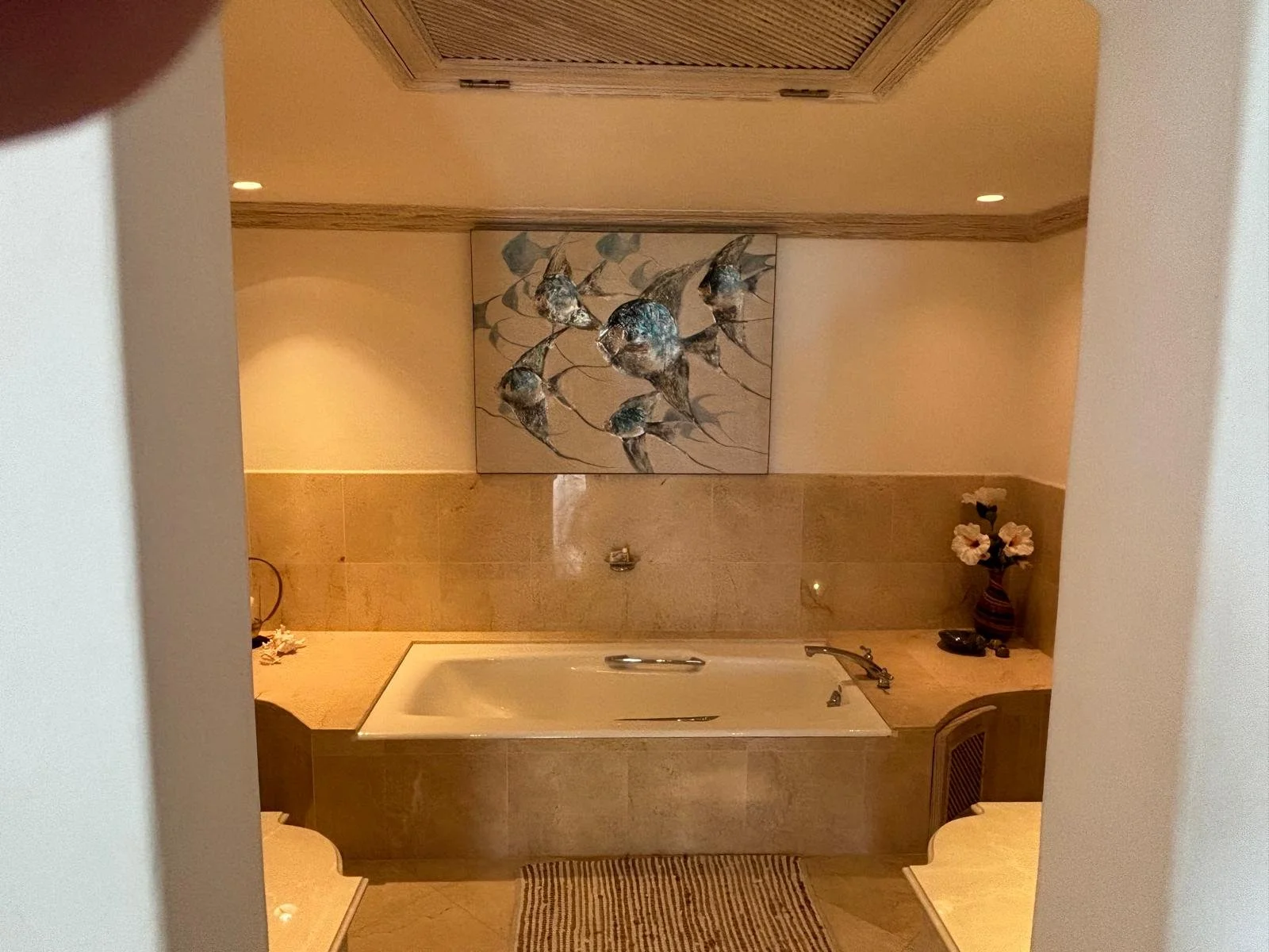 Luxurious bathroom with a recessed bathtub, artwork on the wall, and decorative flowers in a vase.