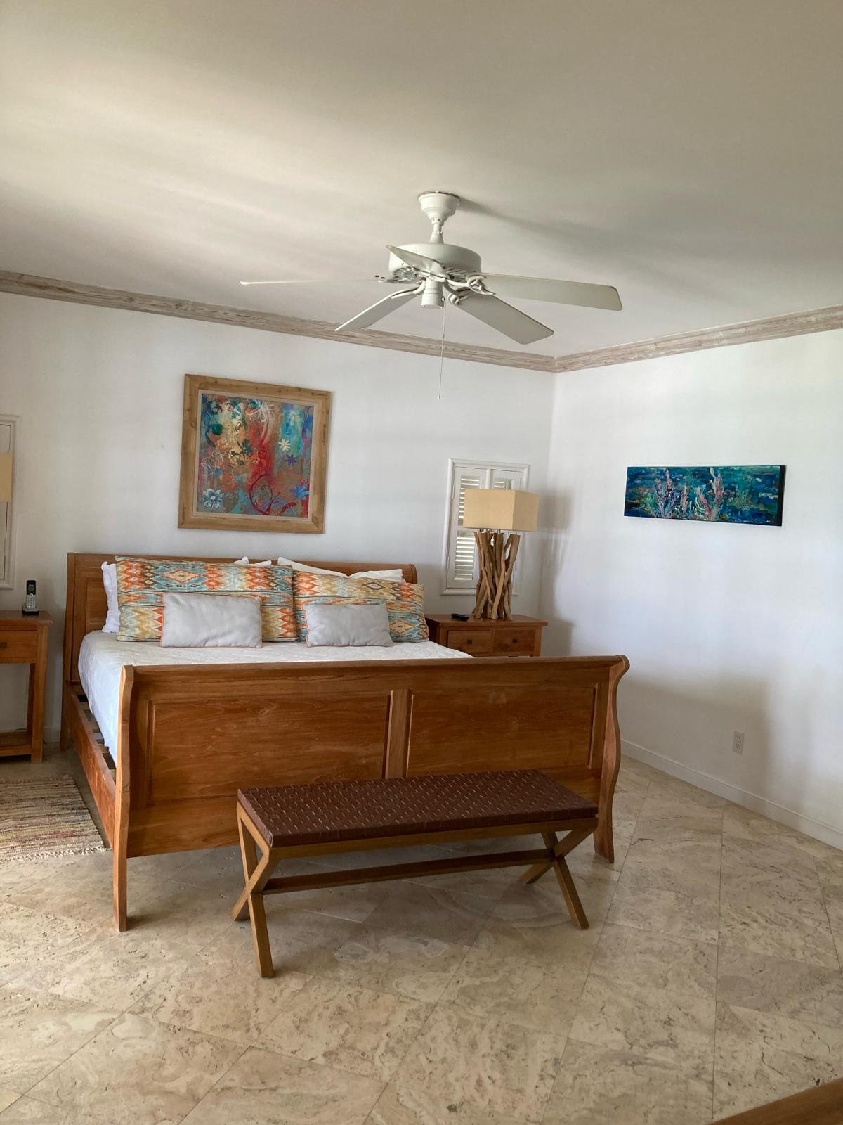 Bedroom with wooden bed, ceiling fan, colorful artwork, and bench
