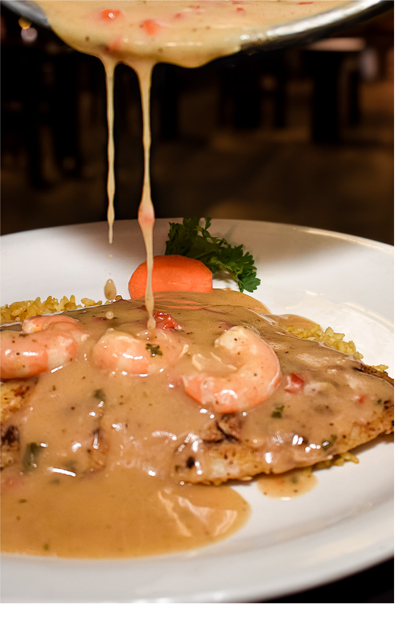 Sauce and shrimp being poured over a fish filet for the Flounder Nueces Bay