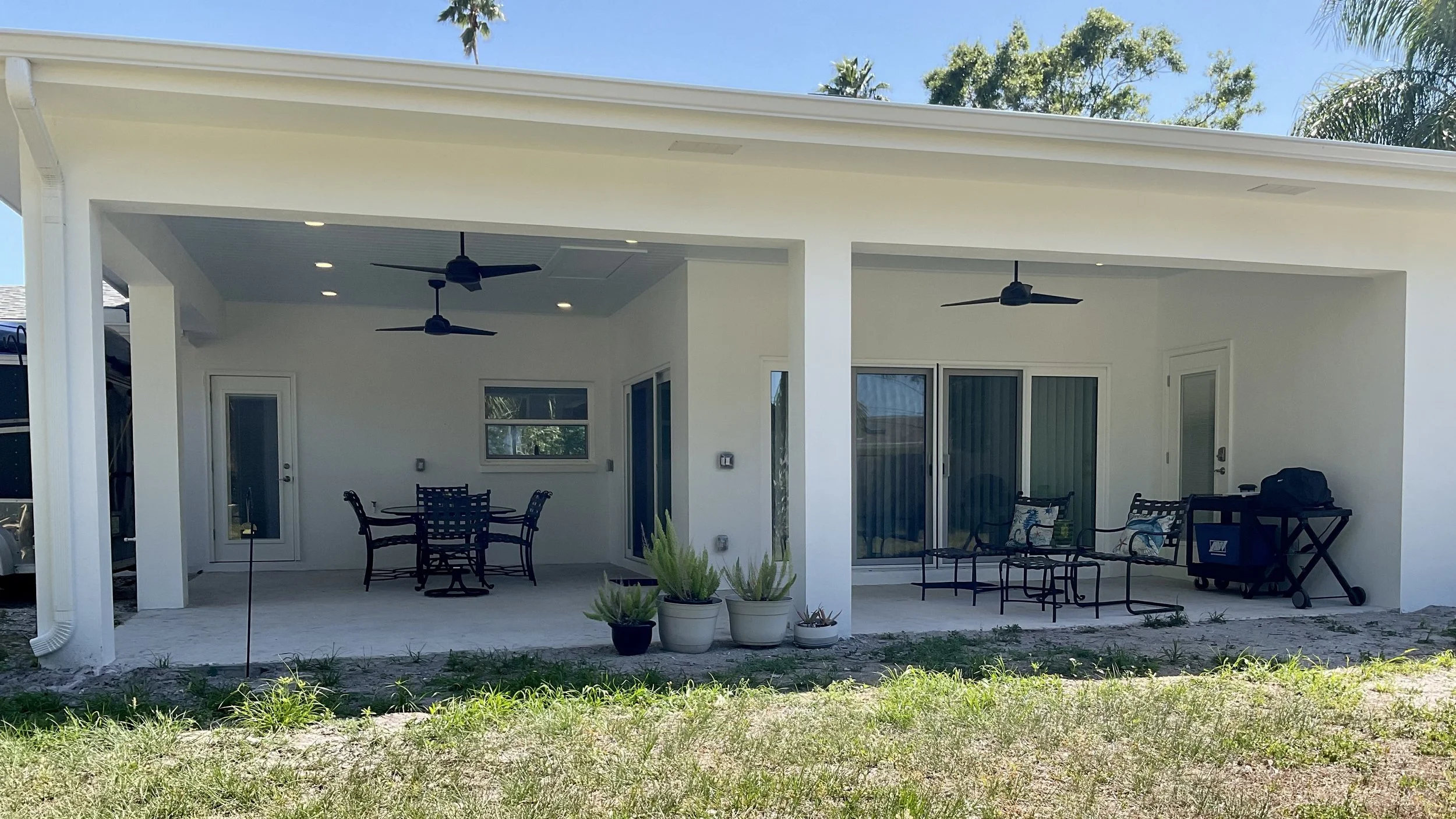 View of lanai from backyard showing stucco columns and beams, ceiling fans, and space for outdoor living; grass area will become future pool deck.