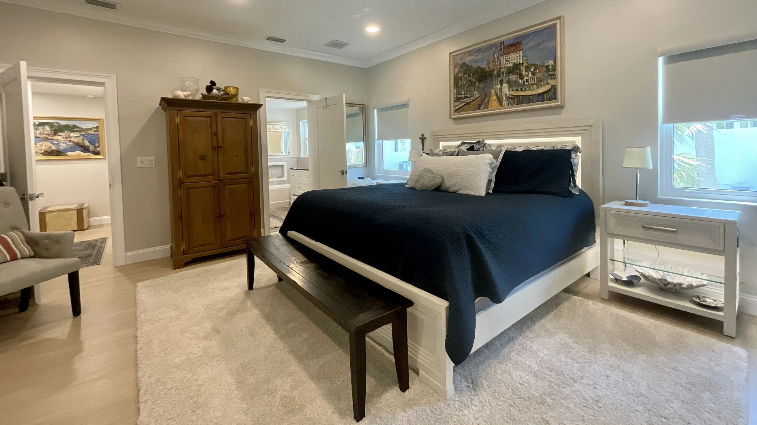Bedroom with 10-foot ceilings, large bed flanked by windows, door to hallway, and door to master bathroom.