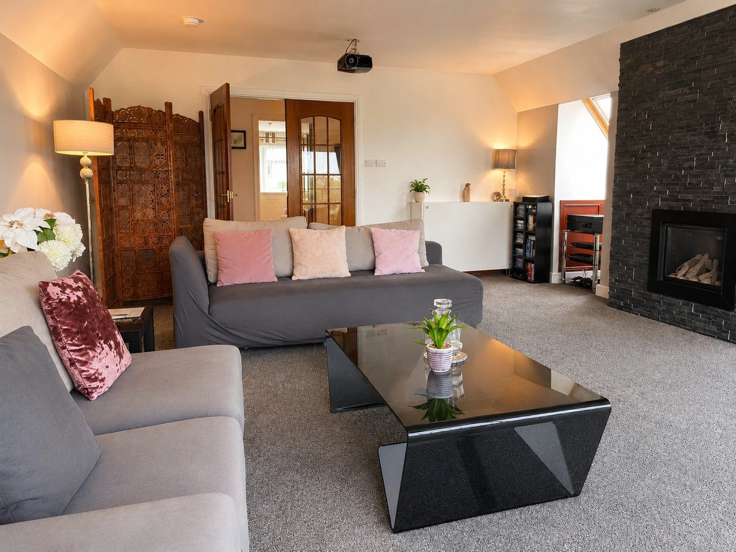 Living room with sofas, a black coffee table with a flower pot, a fireplace with black stones, and various lamps and decorative items.