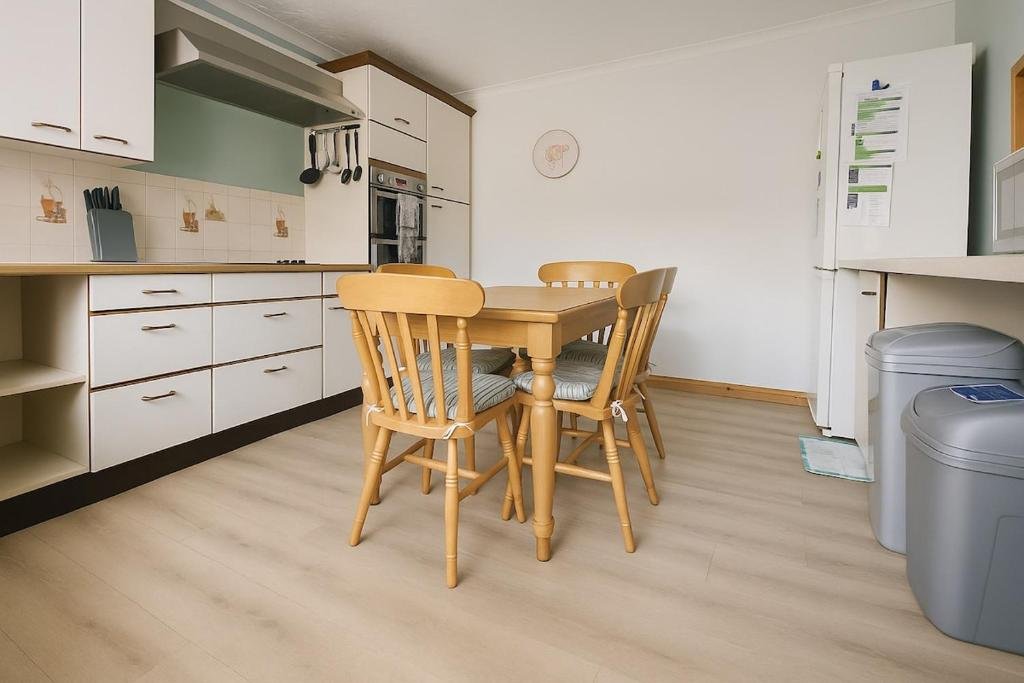 A kitchen with white cabinets, a wooden dining table, four wooden chairs with patterned cushions, a white refrigerator, and laundry baskets.