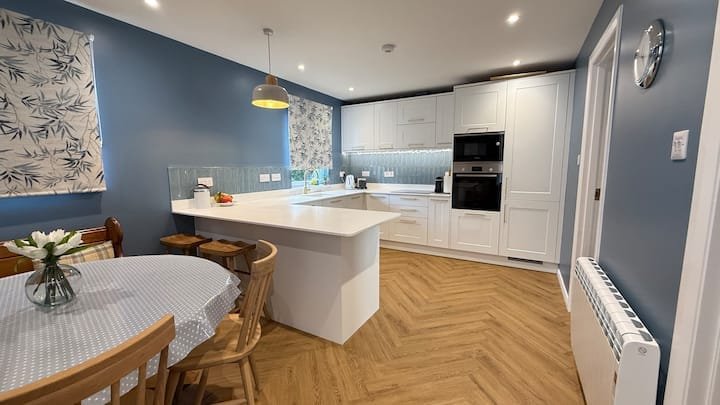 Modern kitchen and dining area with blue walls, white cabinets, wooden flooring, and a round dining table with chairs.