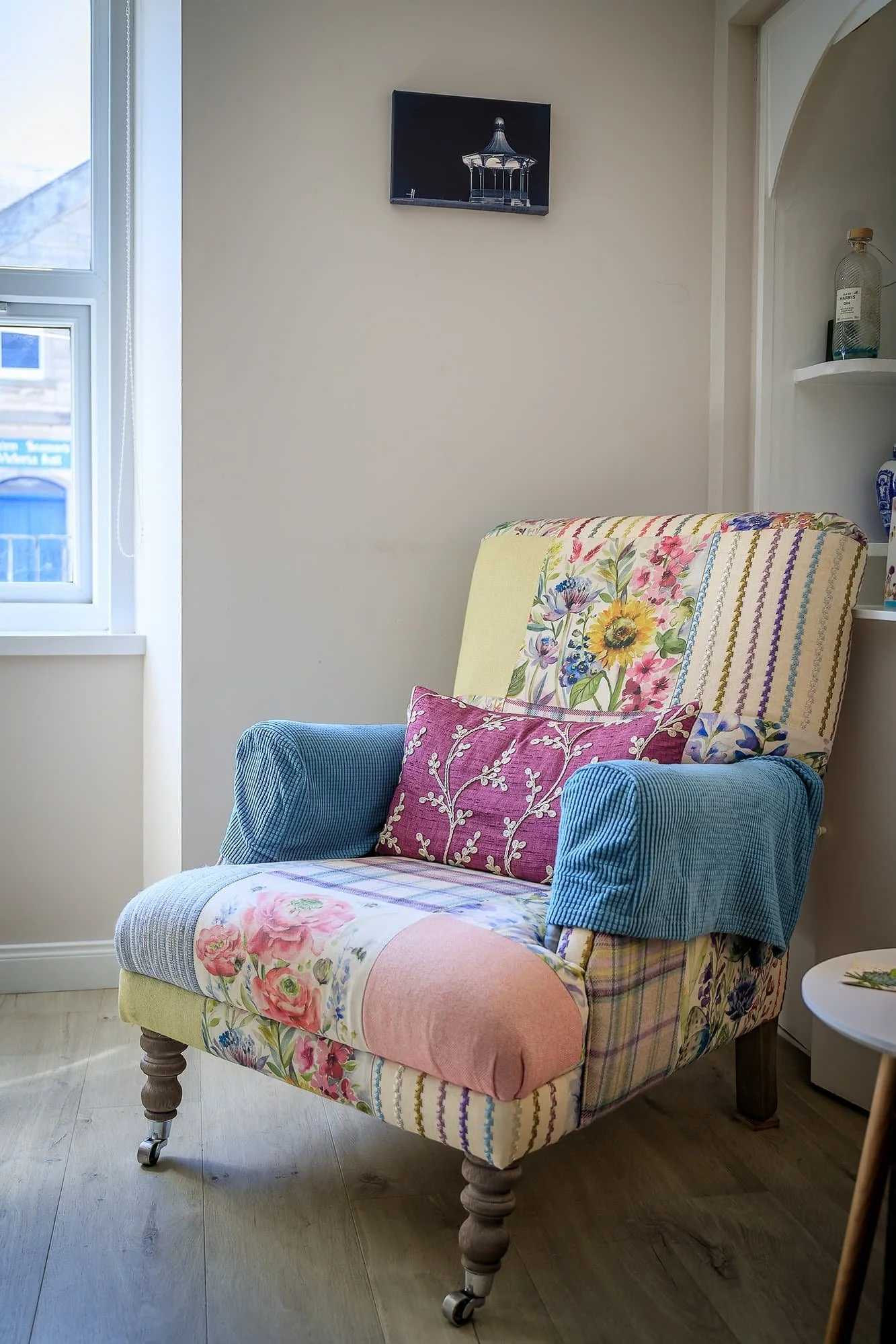 An armchair with floral, striped, and patchwork fabric in a softly lit room, next to a window.