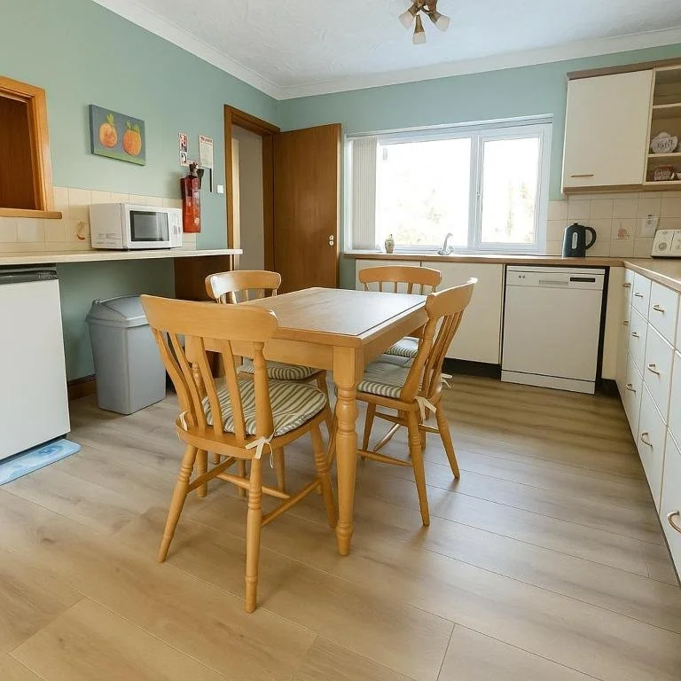Kitchen with wooden dining table and four chairs, green walls, white cabinets, microwave, dishwasher, and a window with outdoor view.