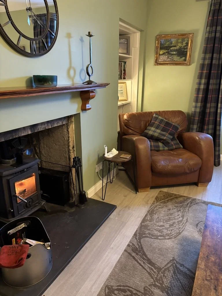 Living room corner with a leather armchair, small side table, fireplace, and wall decorations including a large clock and framed artwork.