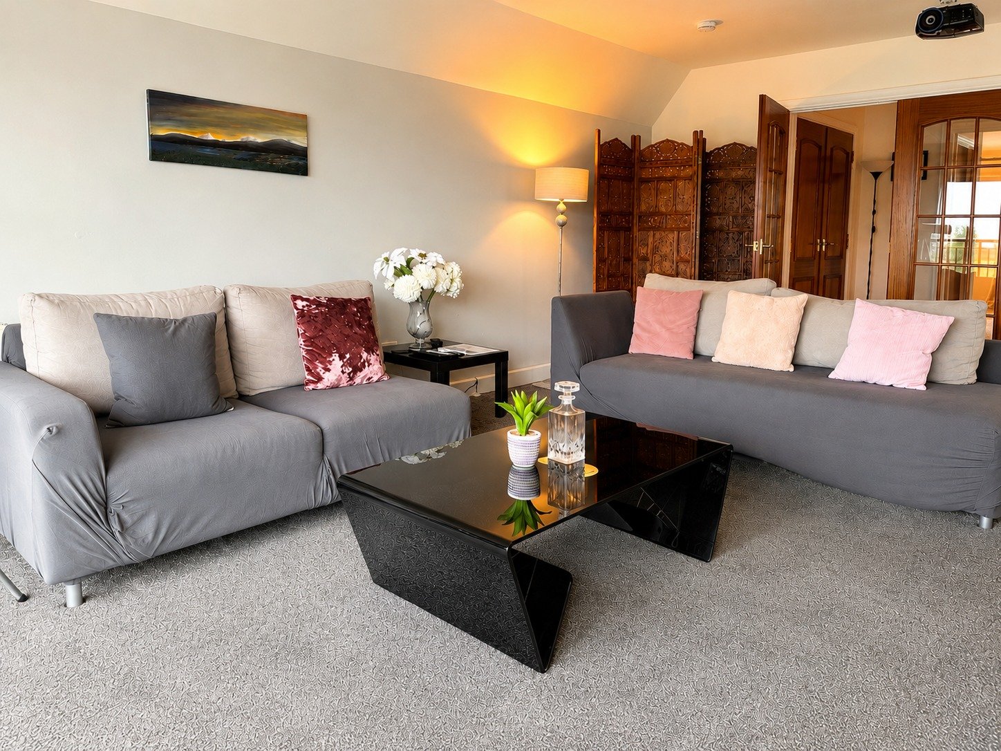 Living room with two gray sofas, a black coffee table, a black side table with a vase of white flowers, a floor lamp, and a wooden room divider.