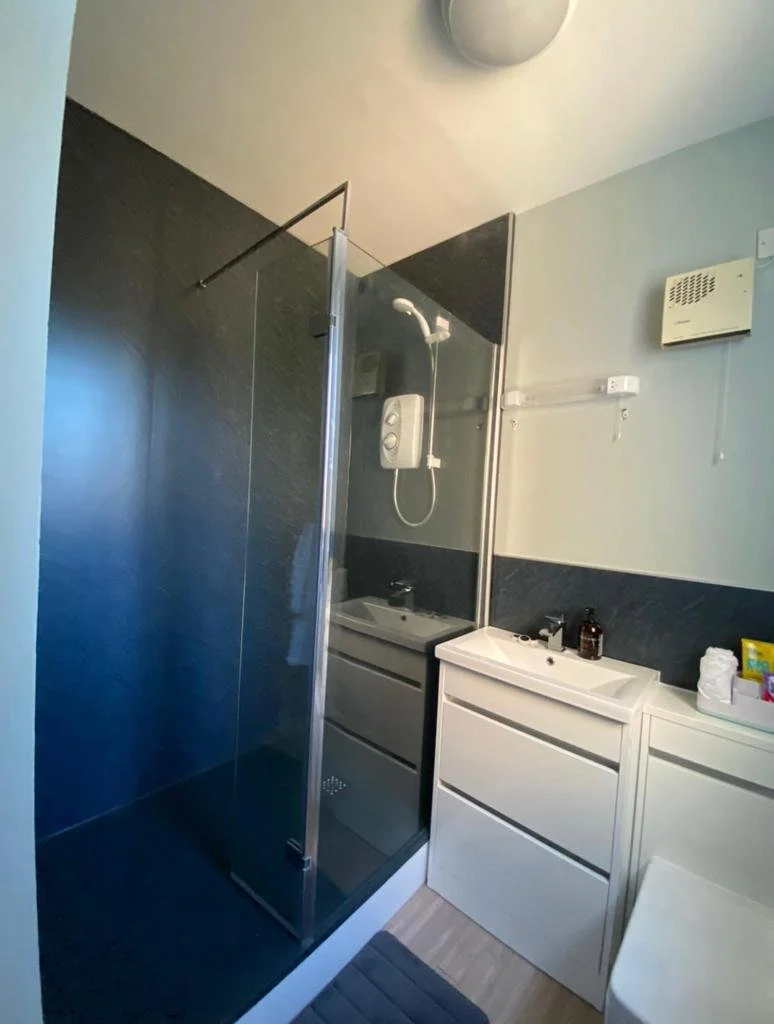 Small bathroom with a glass shower enclosure, a white sink with a cabinet, and a mirror. There's also a white cabinet to the side with personal items and toiletries.