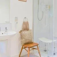 Bathroom with a white sink, a beige tote bag, a patterned pillow, a wooden chair, and a shower area with a glass door.